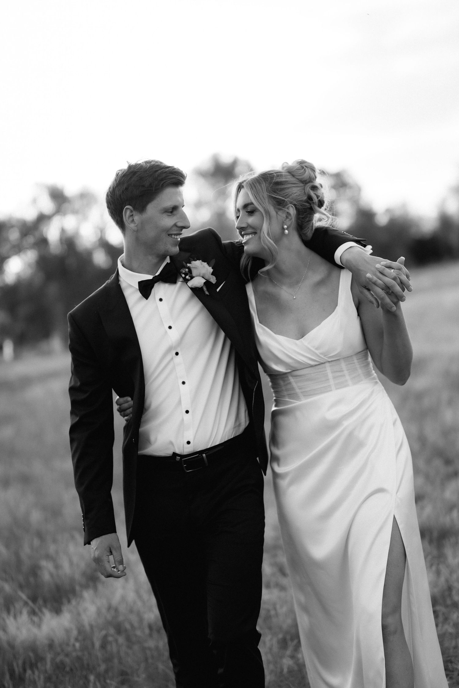 Couple in wedding attire laughing together in a grassy field.