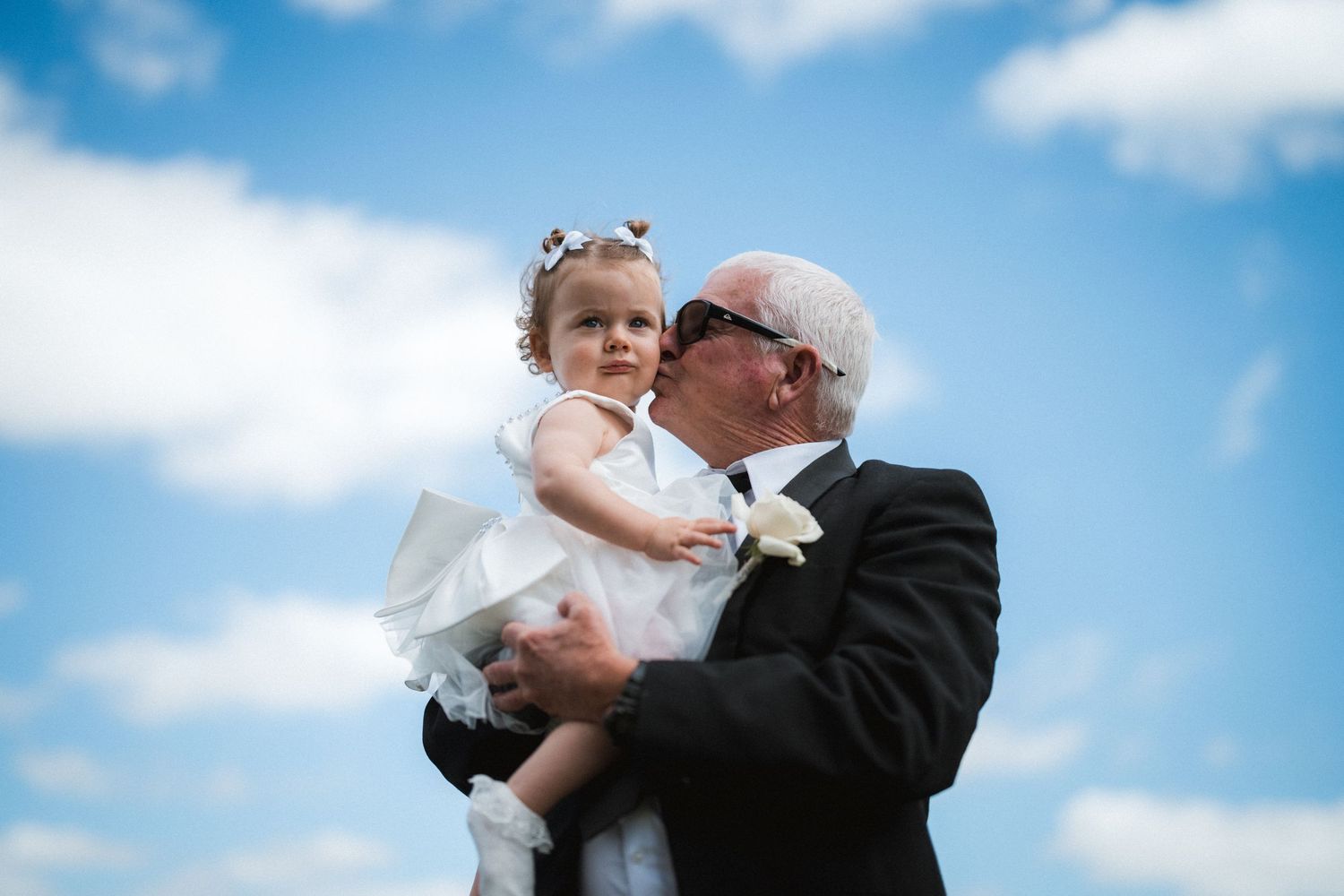 A couple embraces against a bright blue sky during an outdoor celebration.
