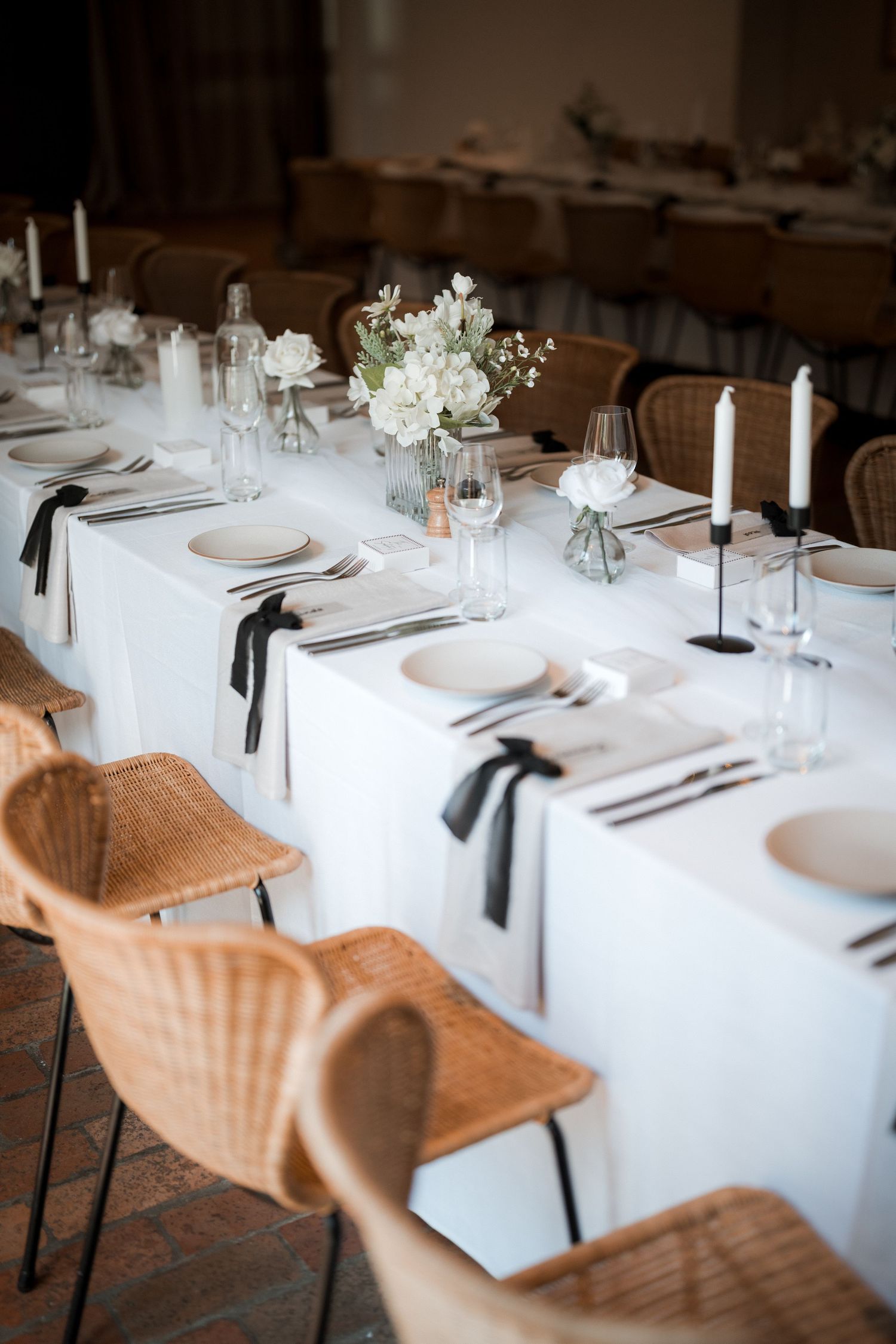 Elegant wedding reception table settings with white linens, delicate place settings, and rattan chairs.