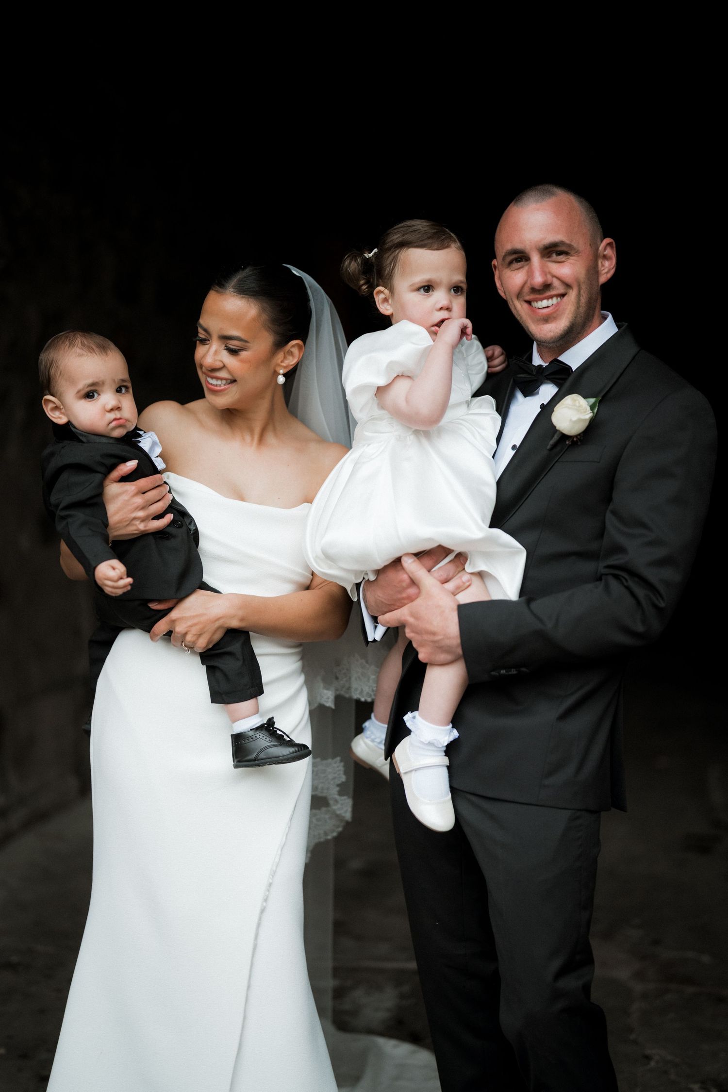Wedding couple holds and plays with a baby dressed in white formal wear.
