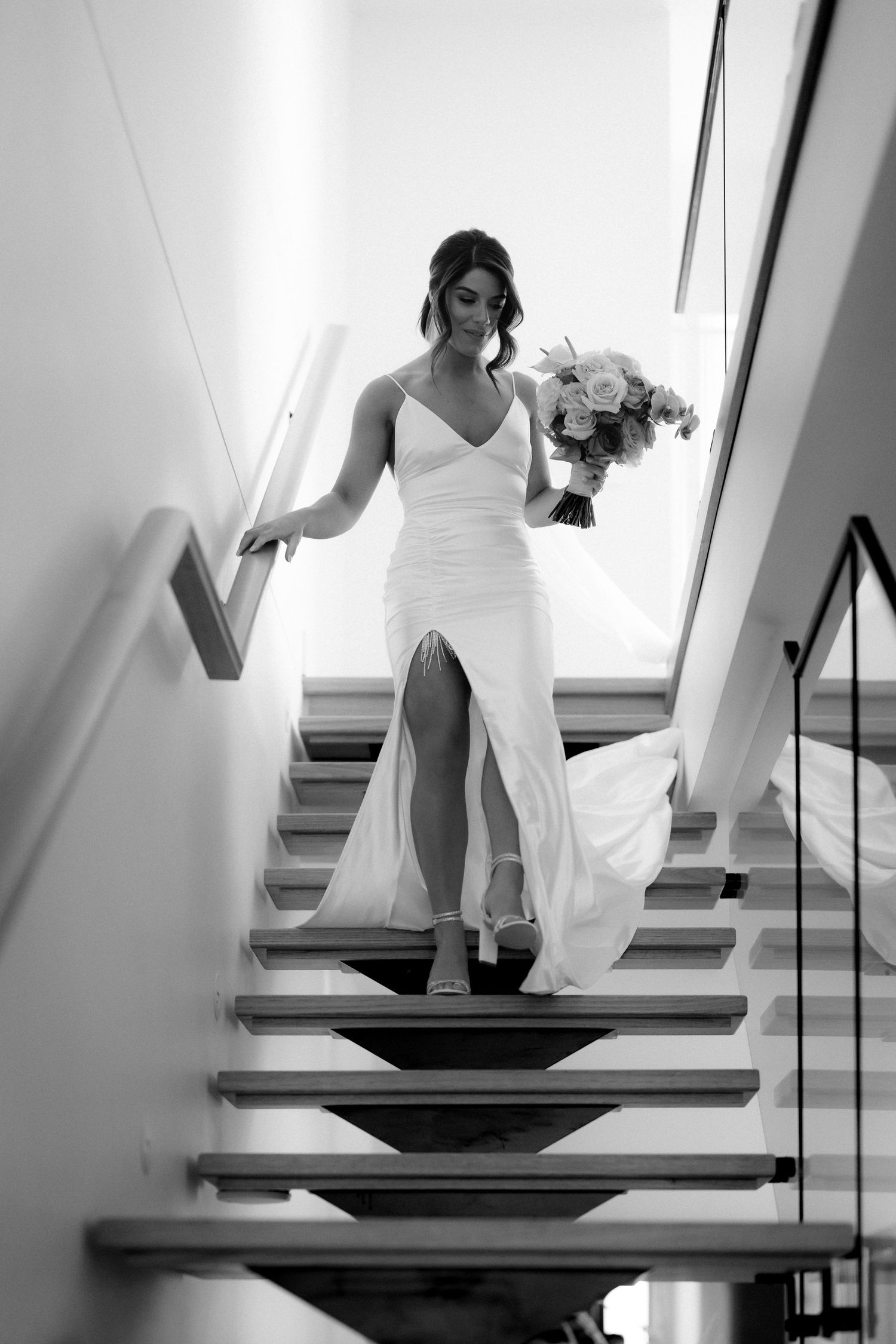 Black and white sequence of a bride descending modern stairs in a white dress.