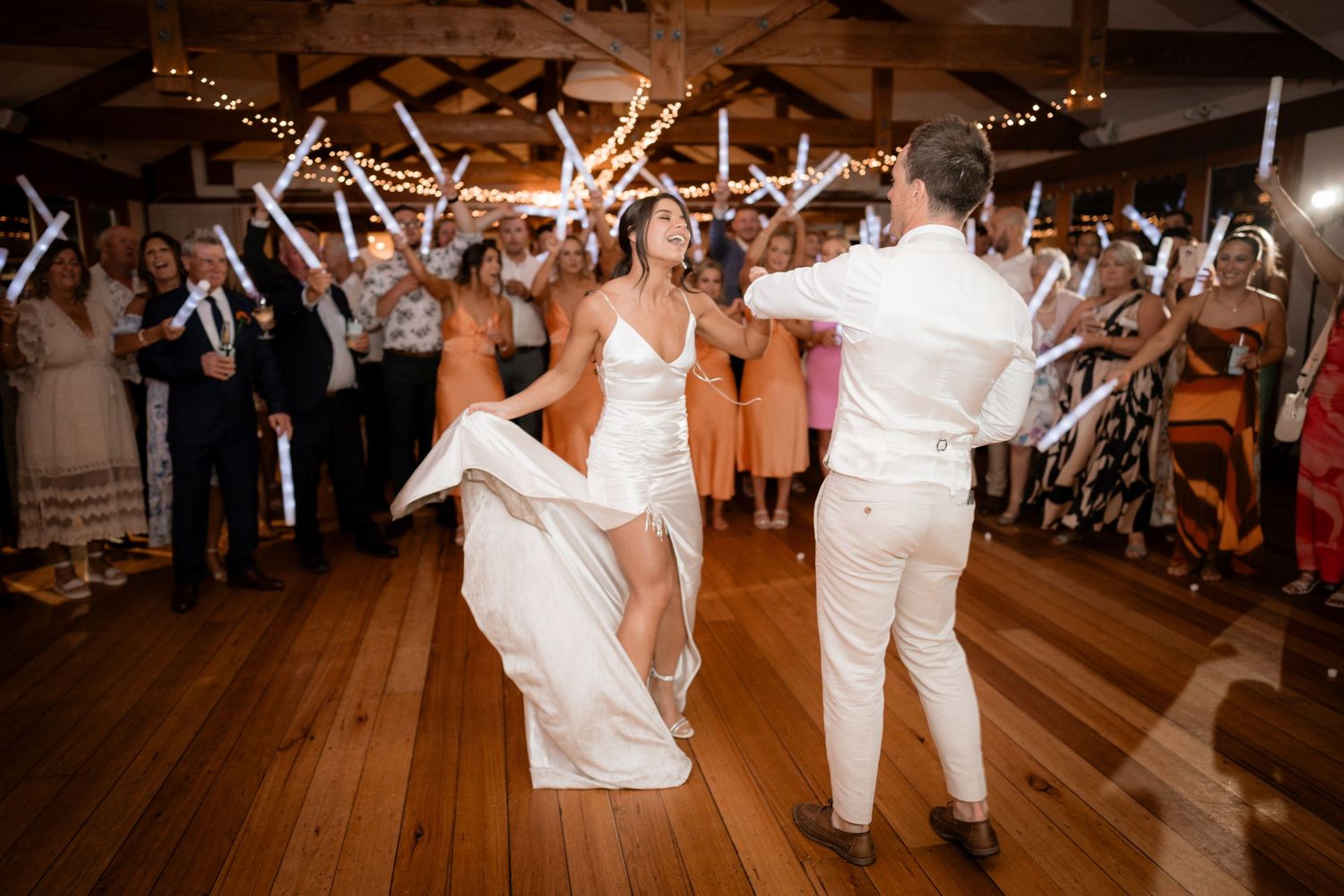 Wedding couple dancing on a rustic wooden dance floor under twinkling lights.