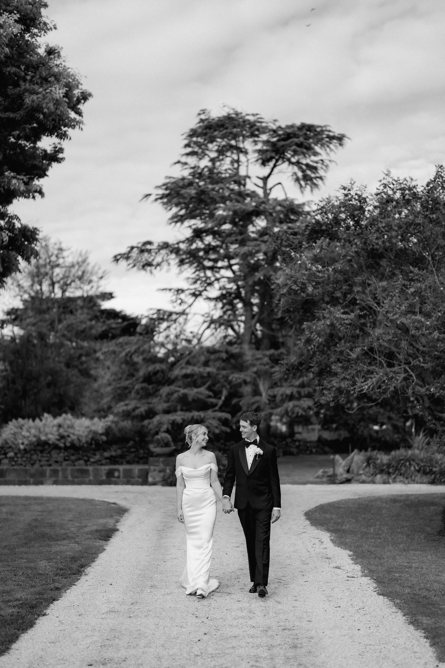 Black and white wedding photos showing a couple walking along a garden path surrounded by trees.