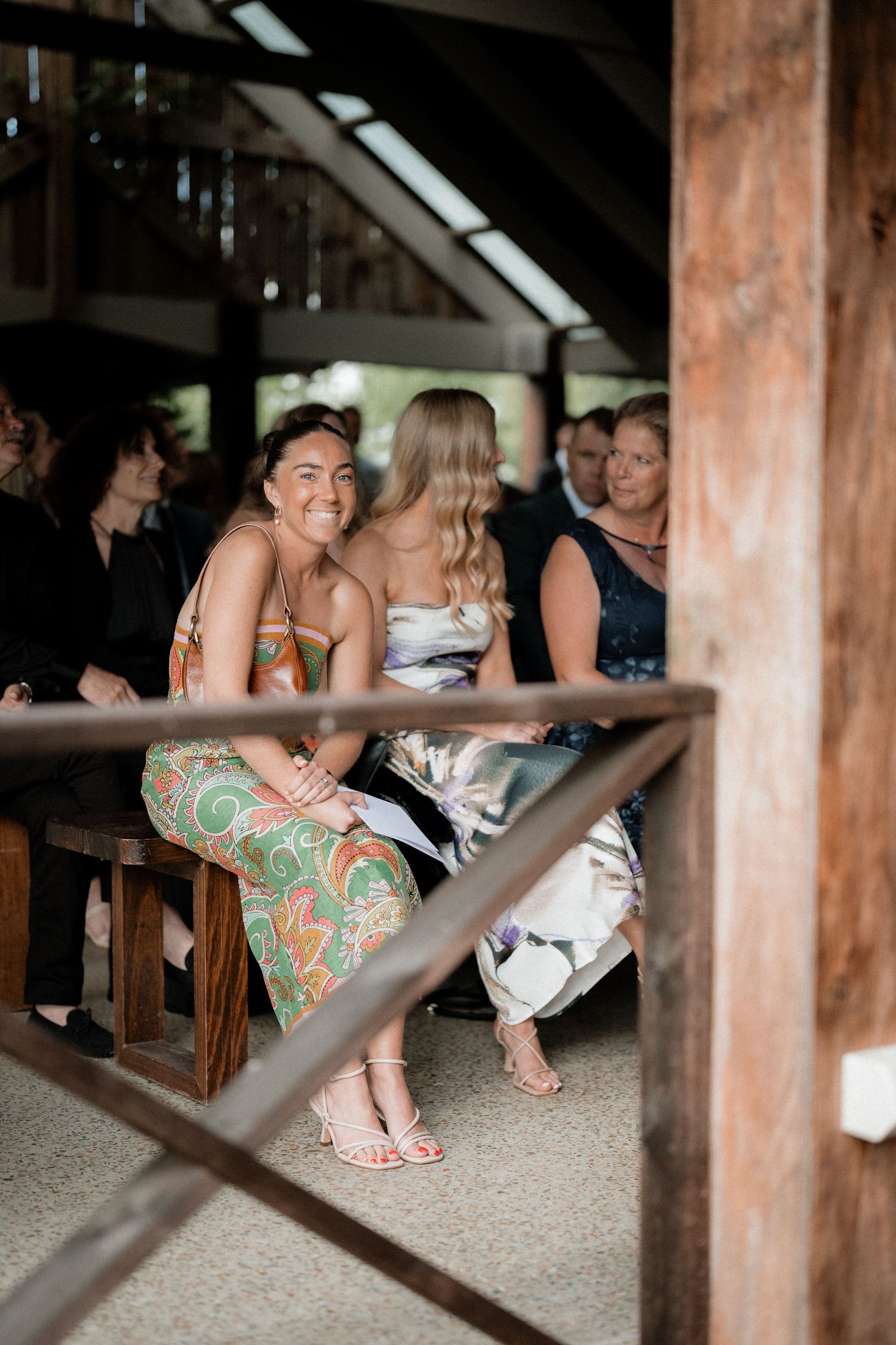 Joyful wedding guests in colorful attire sit at rustic wooden tables during reception celebration.