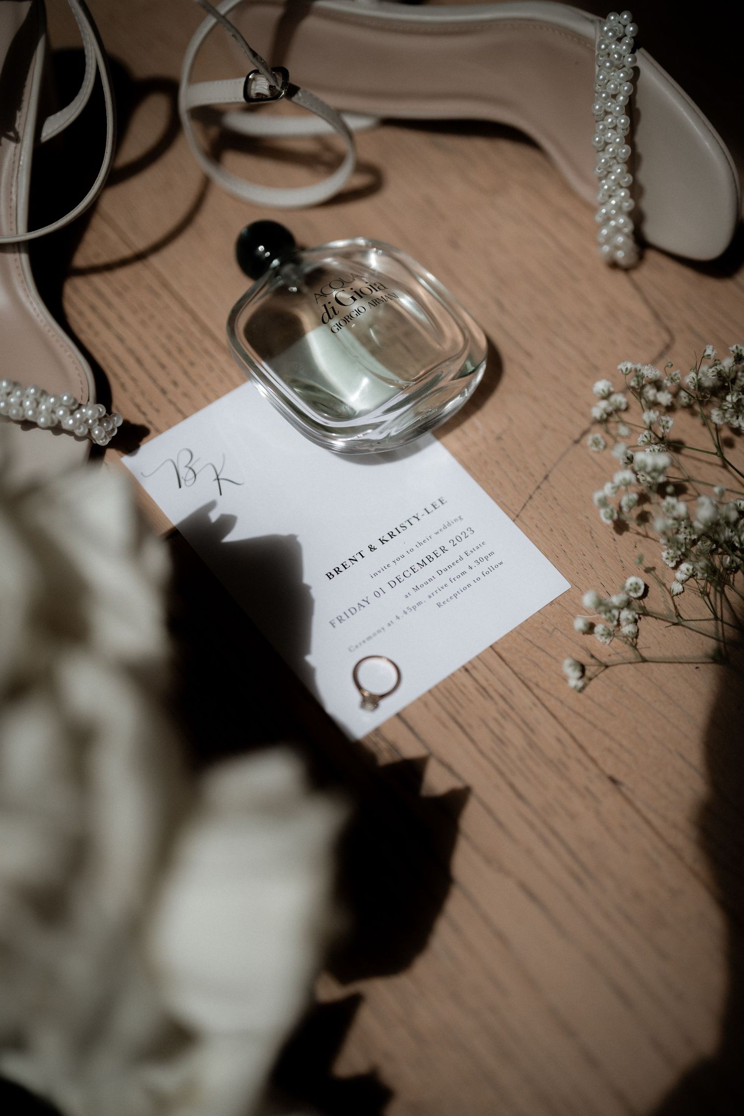Wedding details featuring an invitation card and delicate baby's breath flowers scattered on a wooden surface.