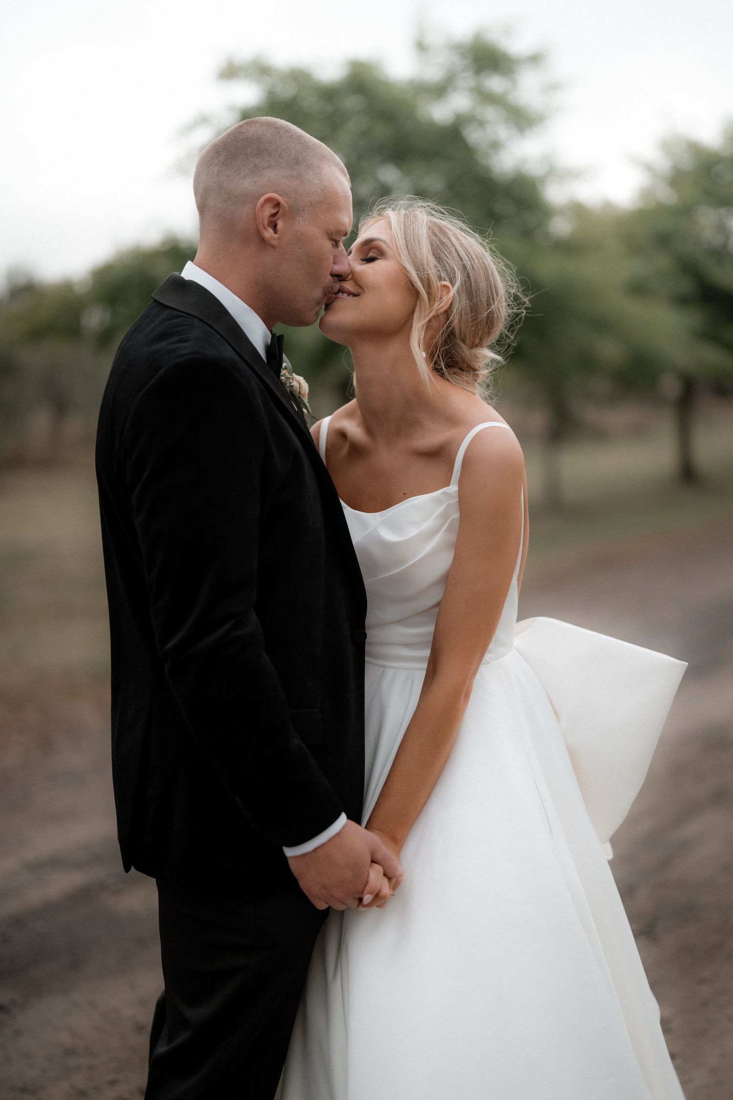 Intimate moment between bride and groom sharing a kiss outdoors in wedding attire.