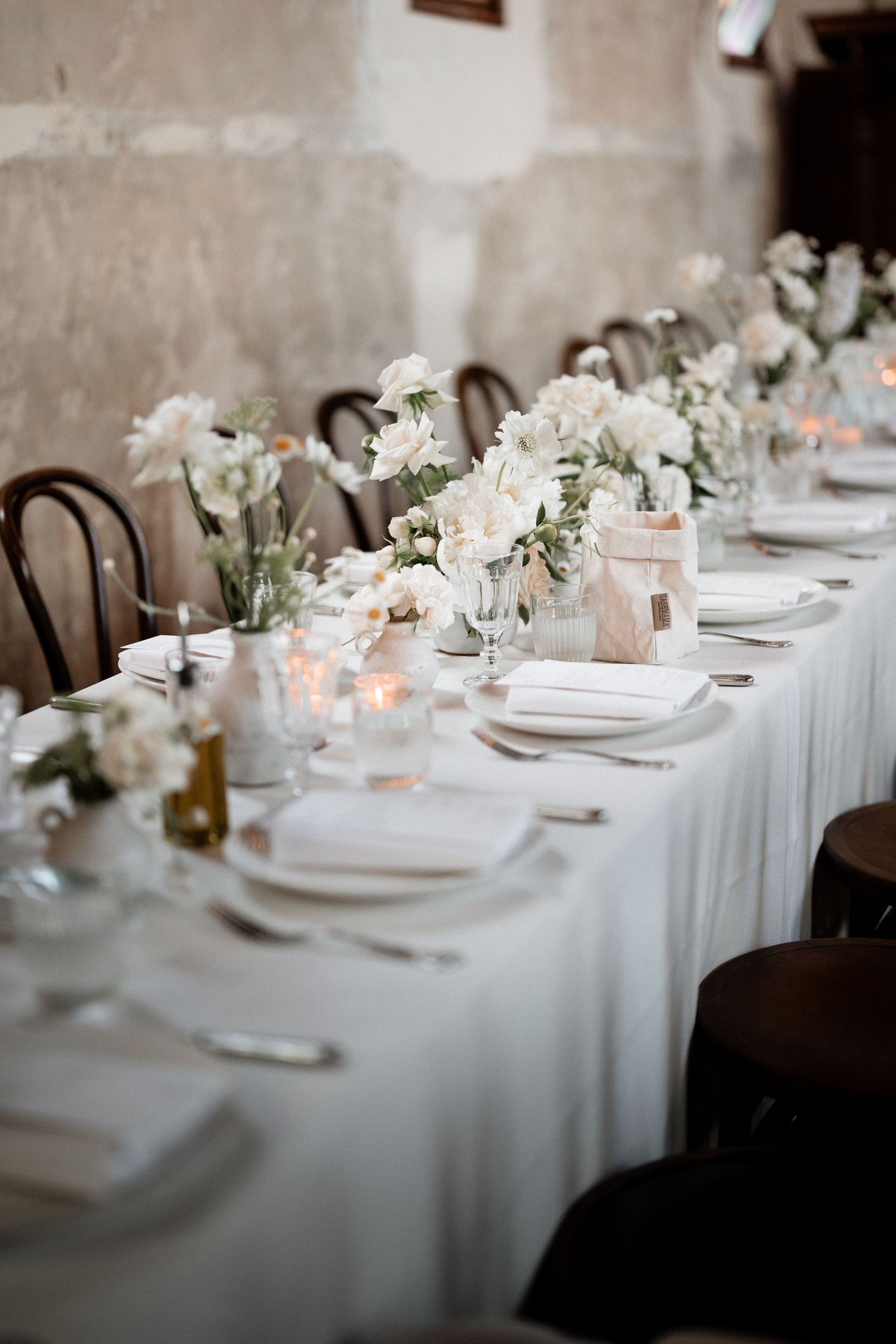 An elegant wedding table setting with white linens, delicate white flowers in vases, and glowing candles creating a romantic ambiance.