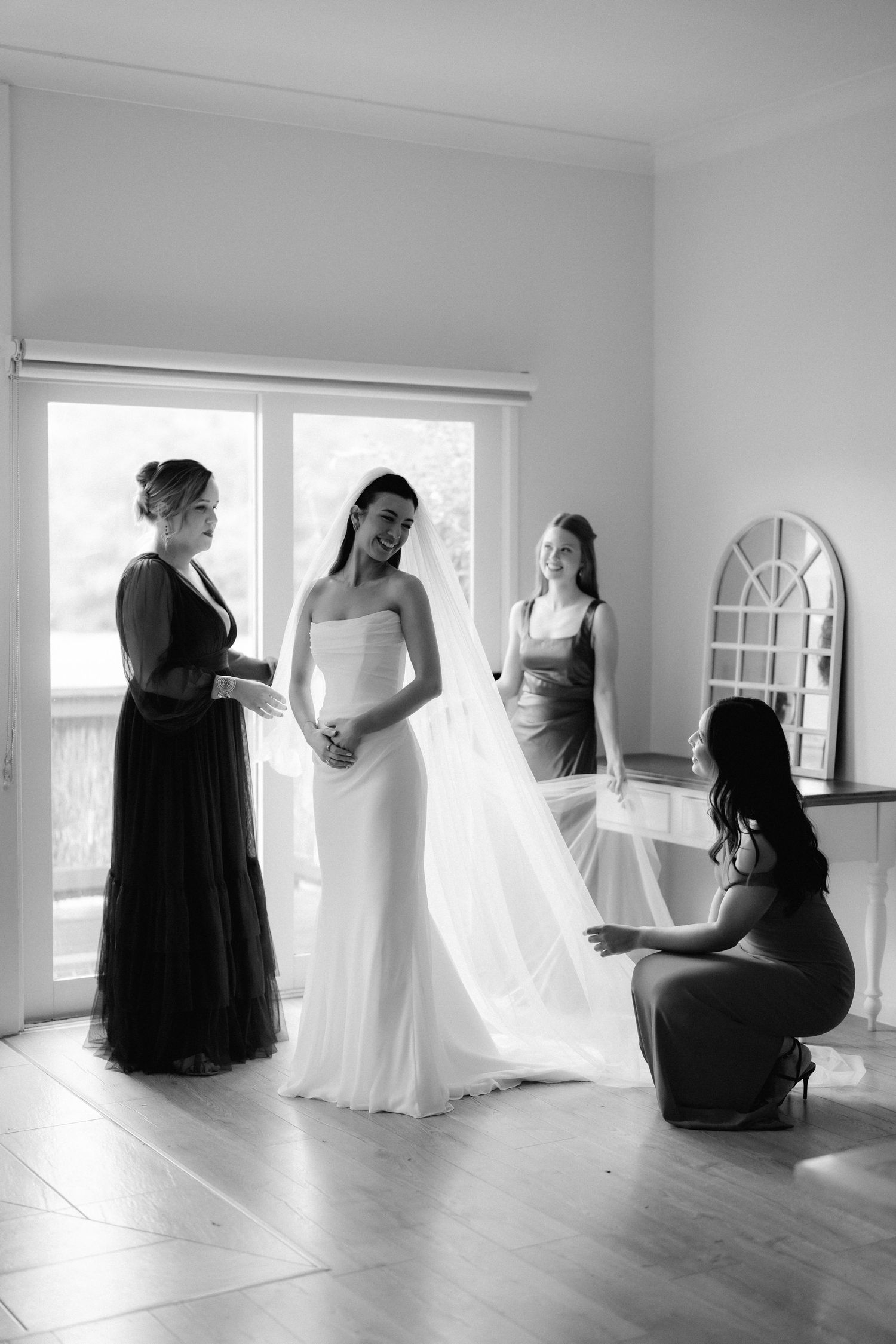 Bridesmaids helping bride with veil in bright white room in black and white photo.