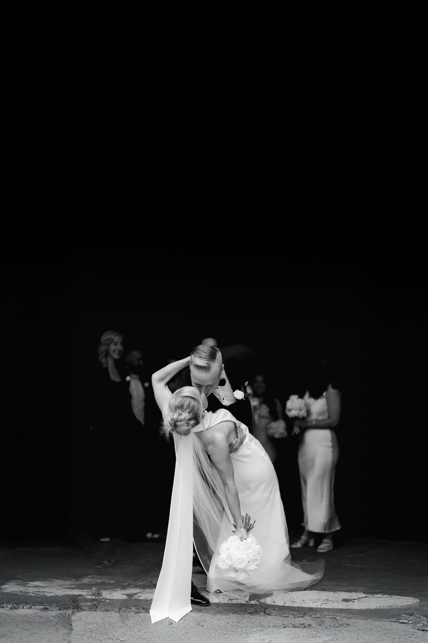 A couple performs a dramatic dip during a wedding dance at night, with the bride's white dress flowing elegantly.