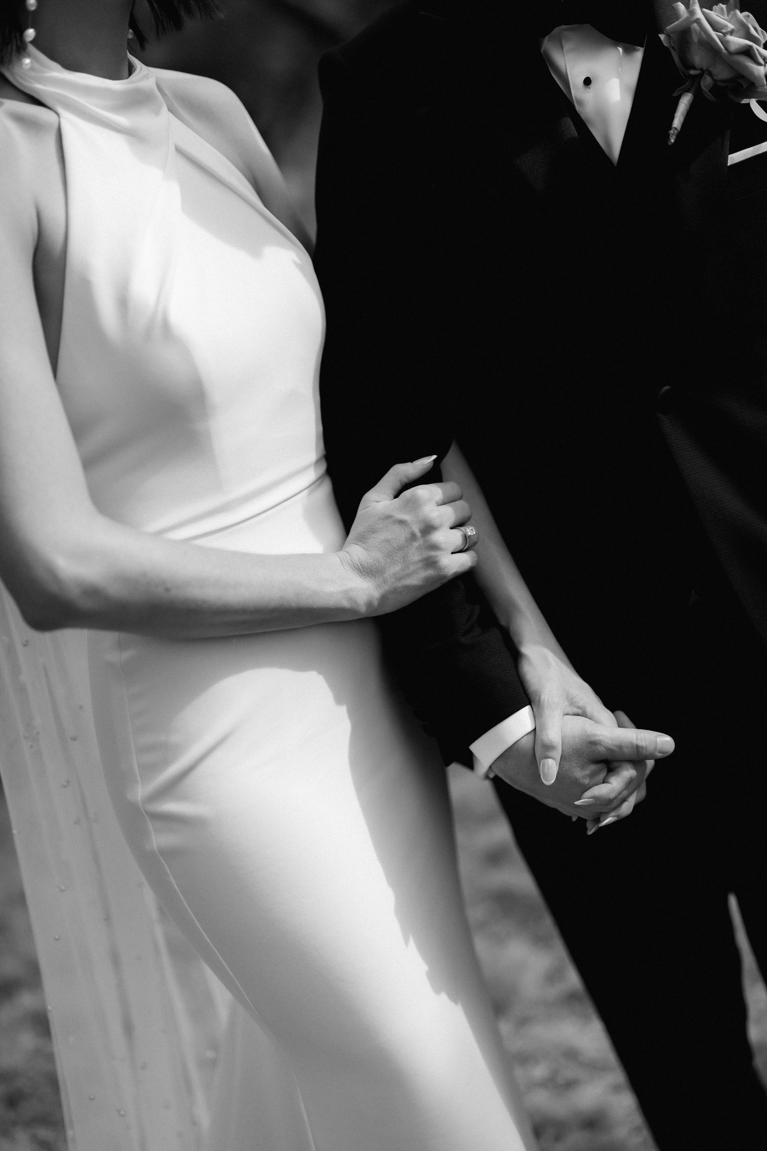 A black and white close-up of a couple's elegant formal attire showing hands and torsos.