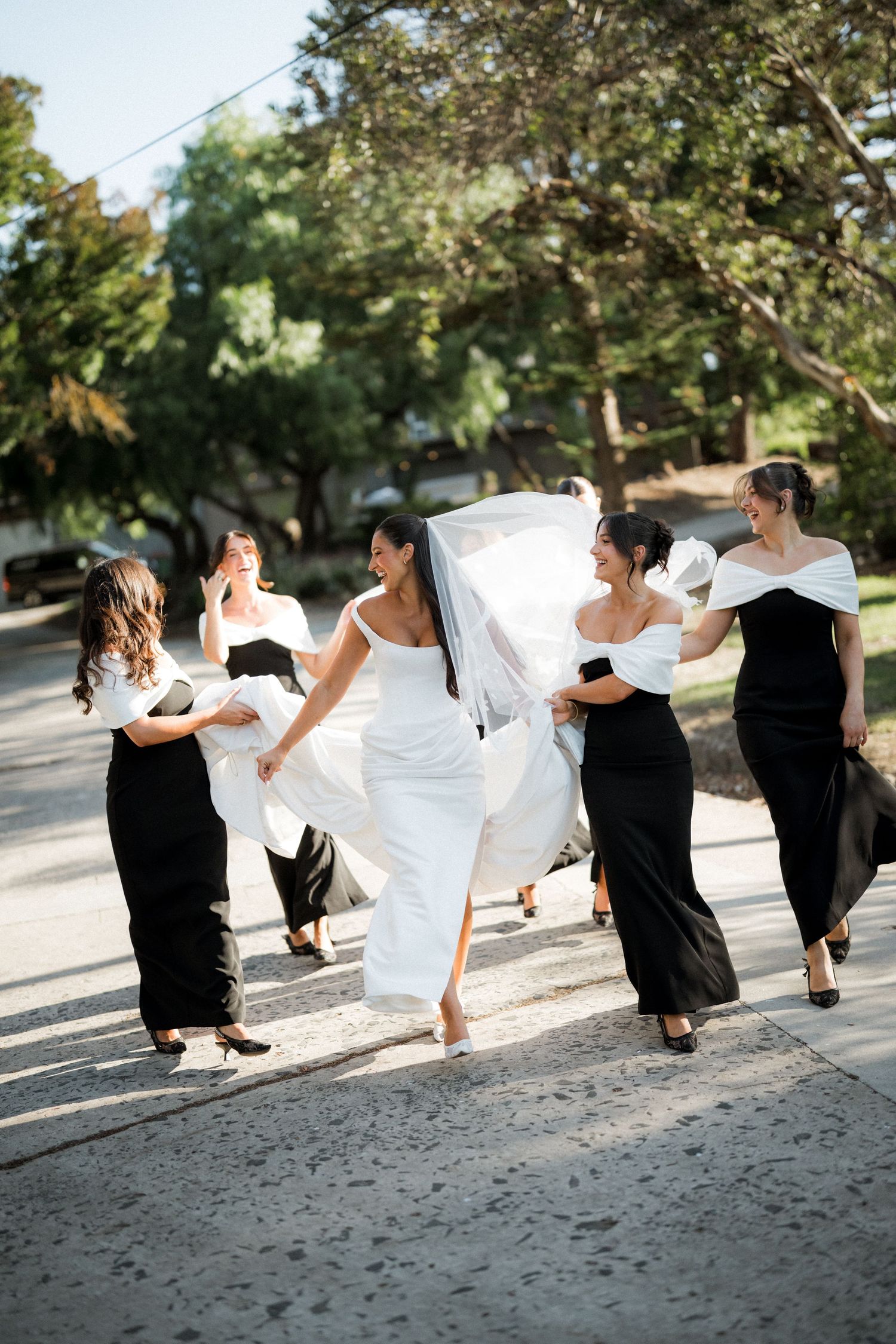 Wedding party in black and white attire poses playfully on sandy beach.