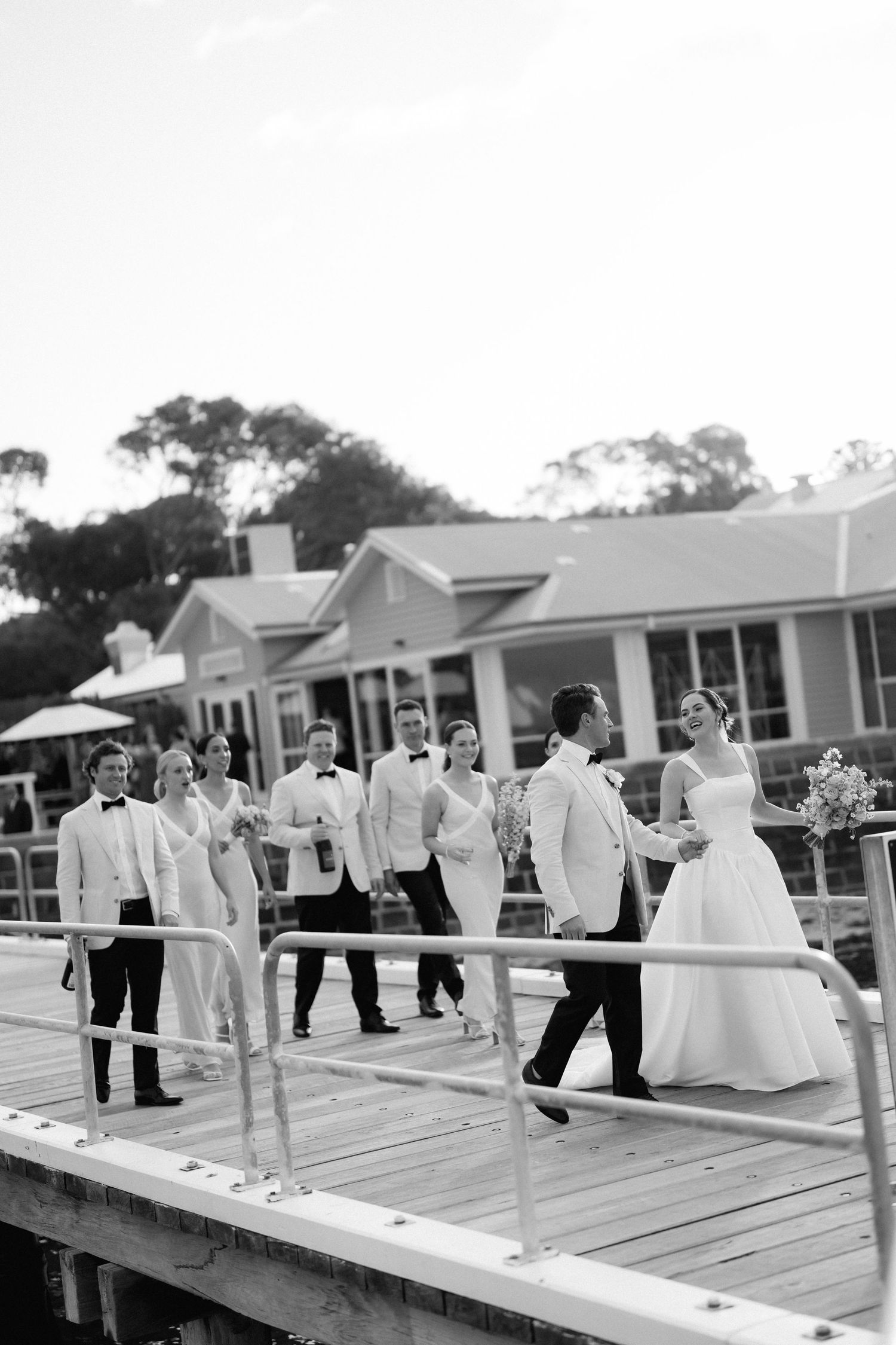 Wedding party members gather on a wooden deck overlooking houses during a celebration.