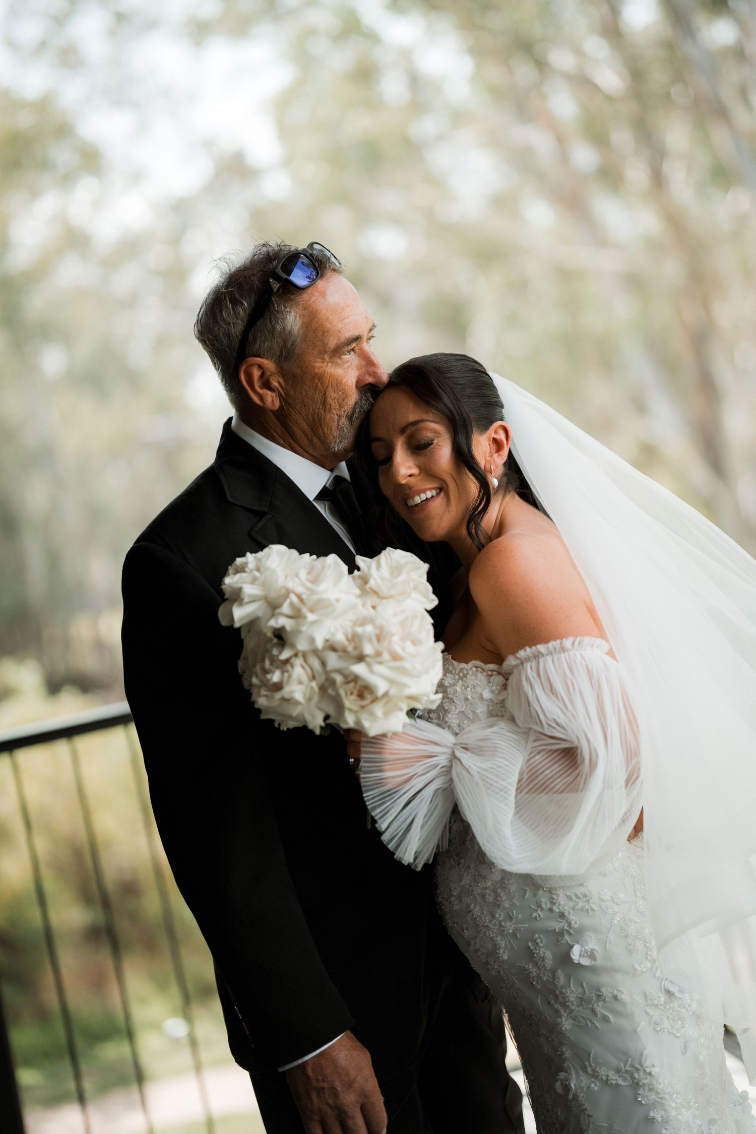 A romantic wedding moment captured outdoors with a bride in white lace and groom in black suit.