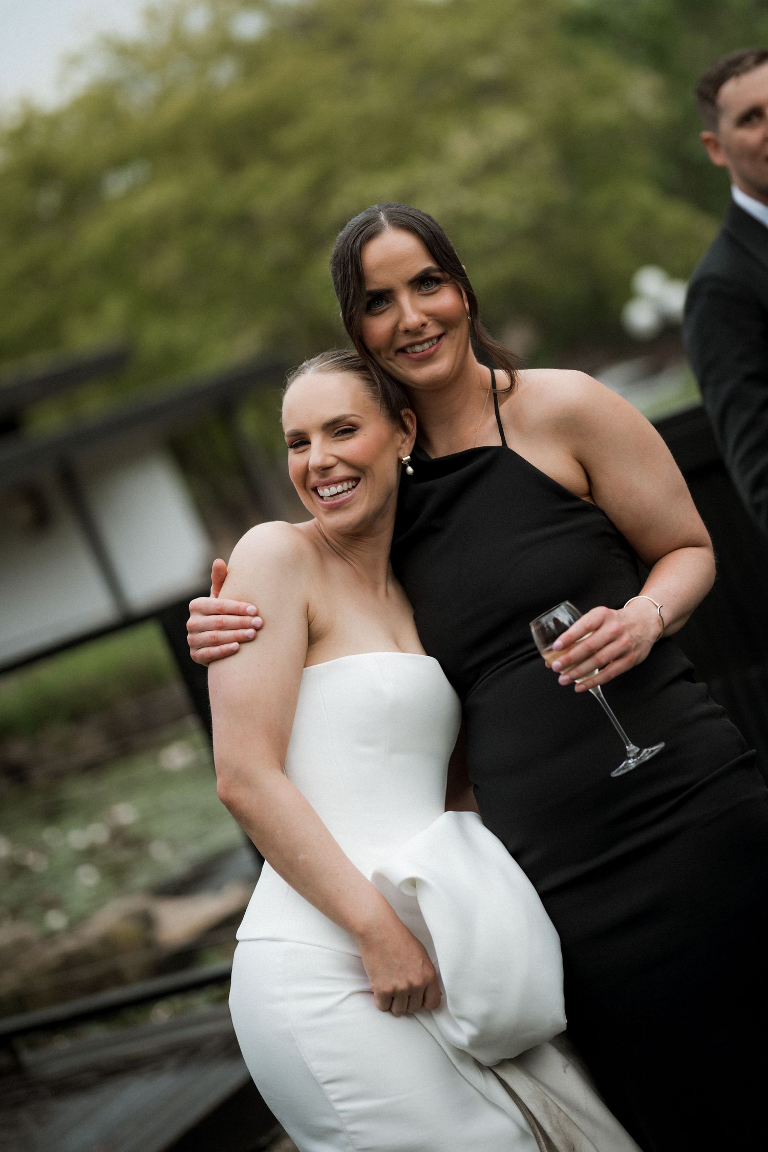 A couple in wedding attire share an intimate moment while holding wine glasses in an outdoor garden setting.