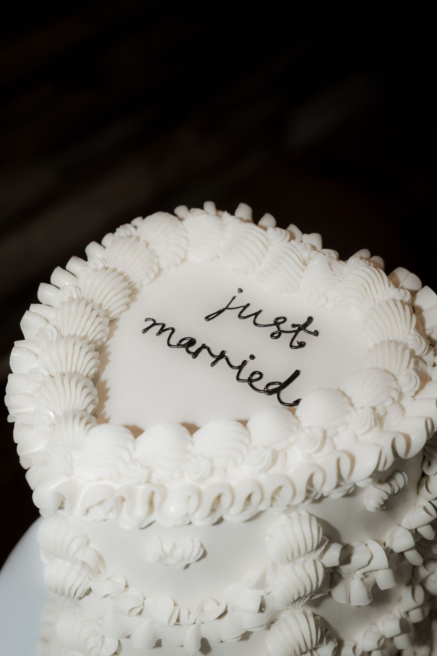 Close-up of a white wedding cake with piped frosting details and 'just married' written on top.