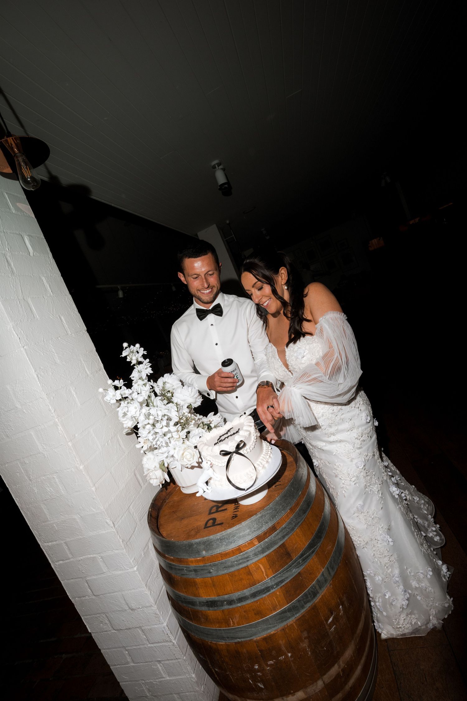 Wedding couple sharing a playful moment near a rustic wooden barrel at night.