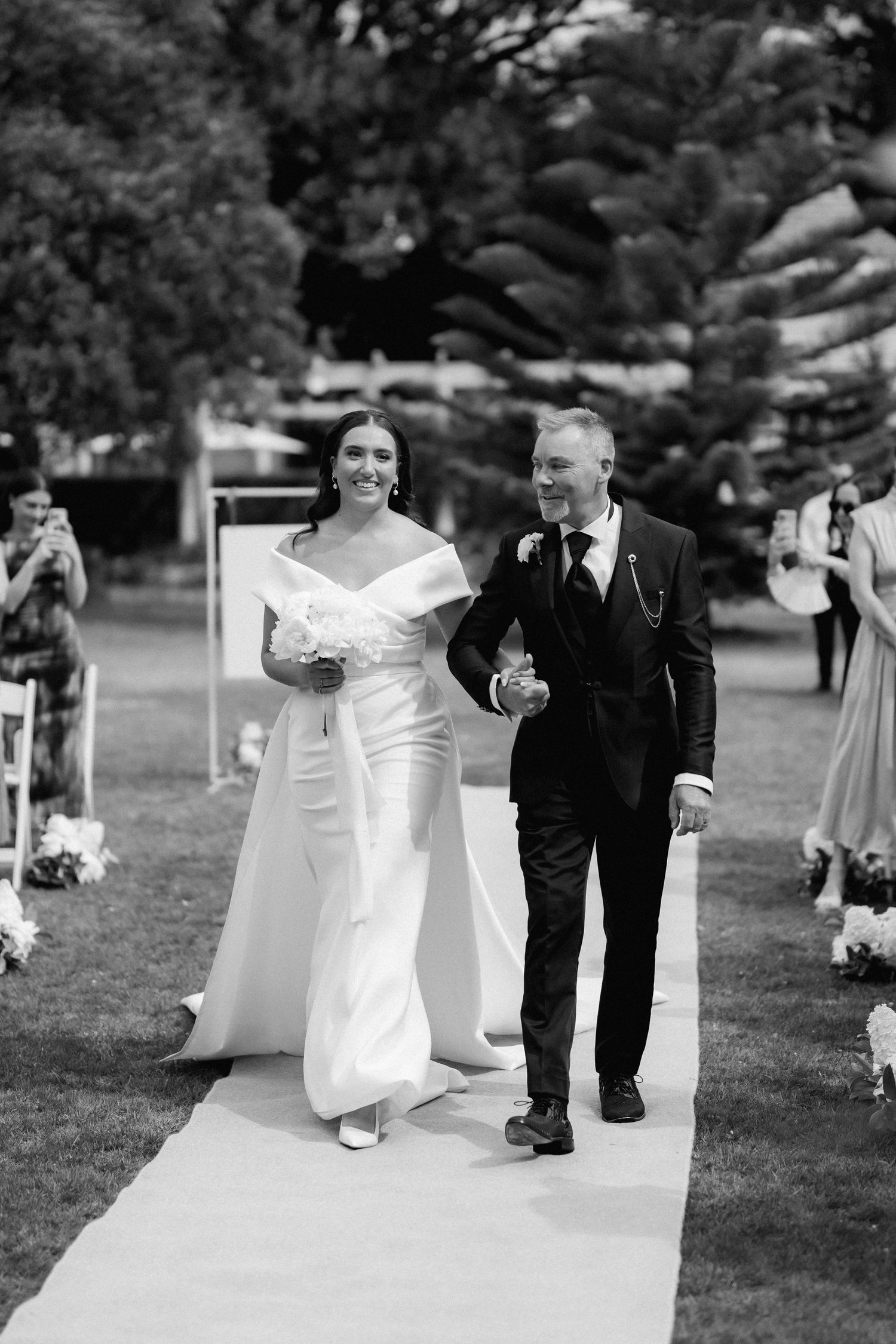 A bride and groom walk down an outdoor aisle during their garden wedding ceremony.