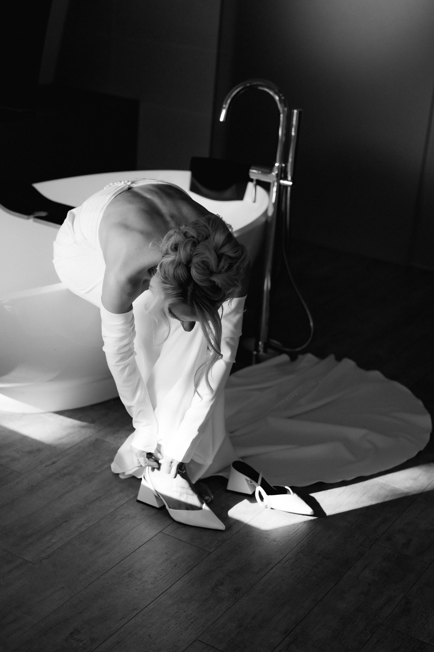 Person in white attire bending down to adjust their shoes on a wooden floor.