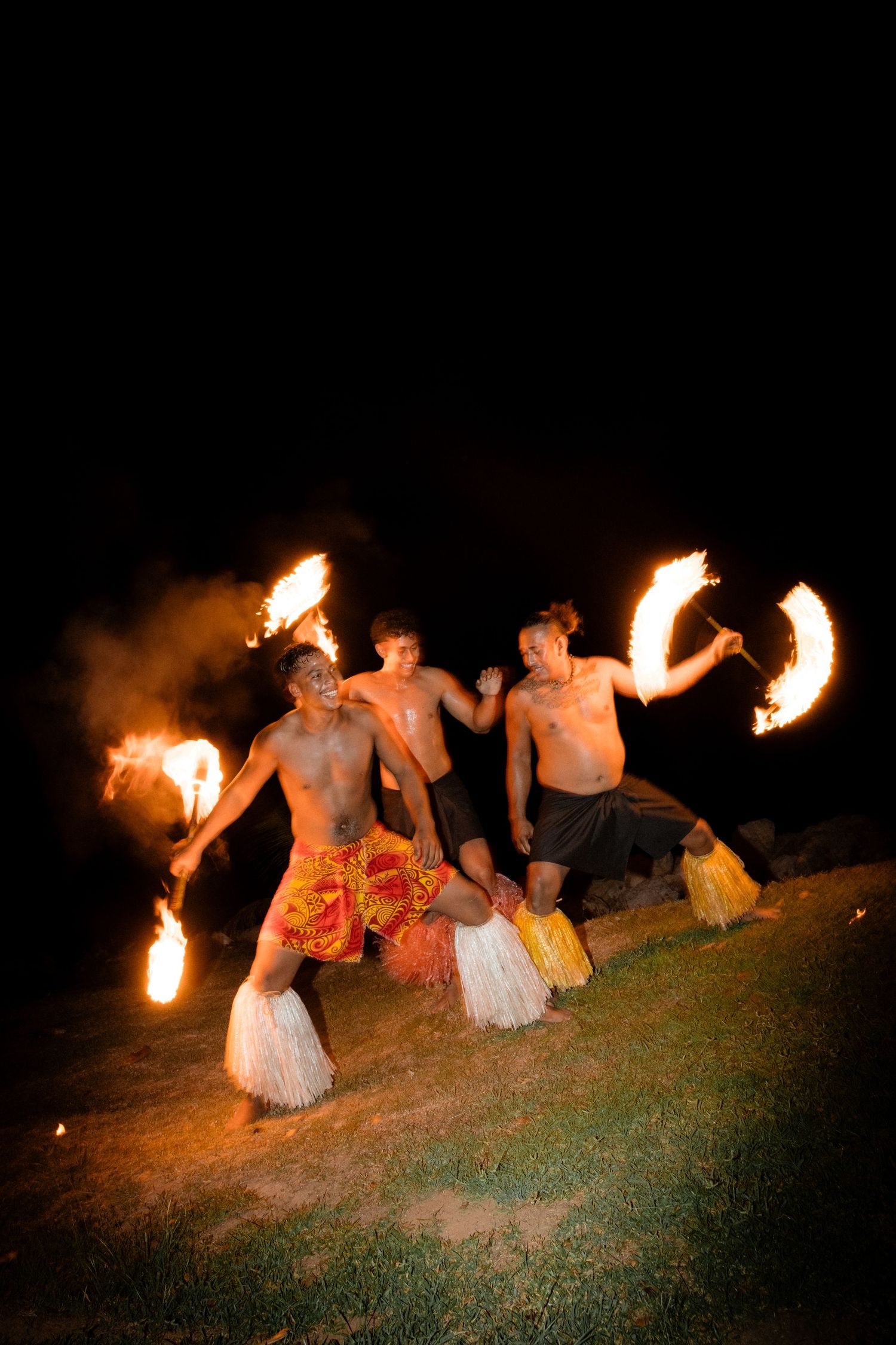 Fire dancers perform with flaming props at night wearing traditional grass skirts.