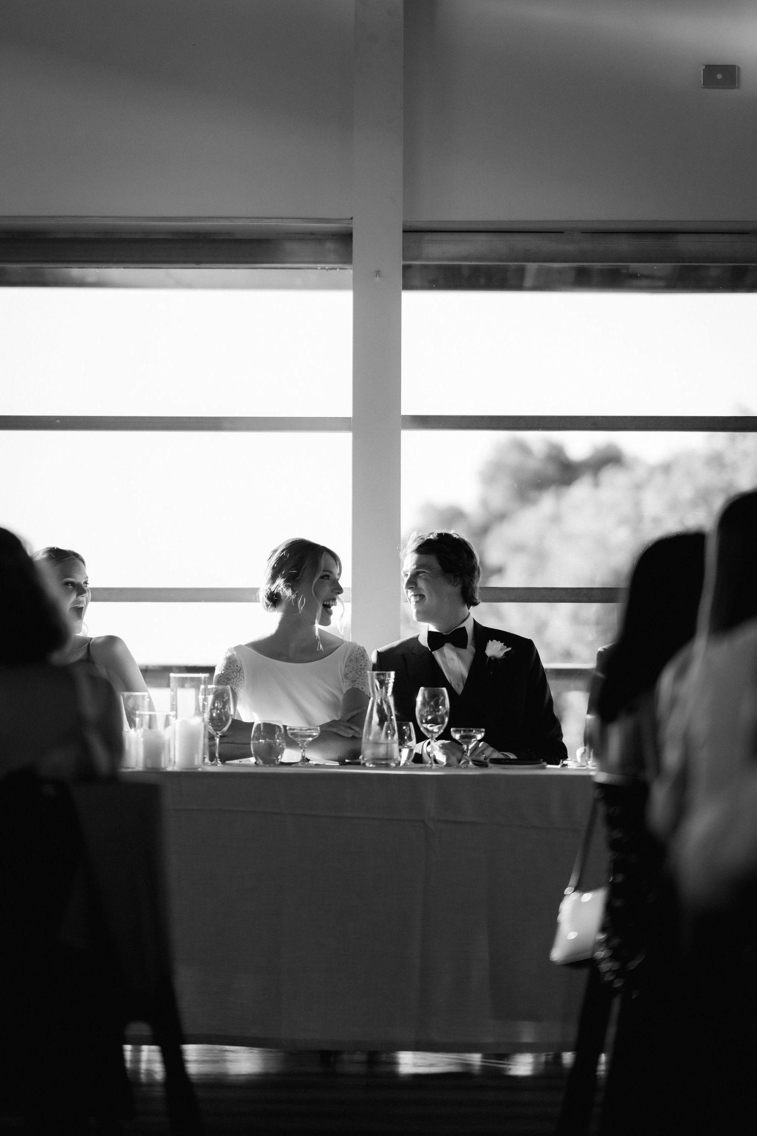 Black and white candid reception photo of couple seated at table with window backdrop.