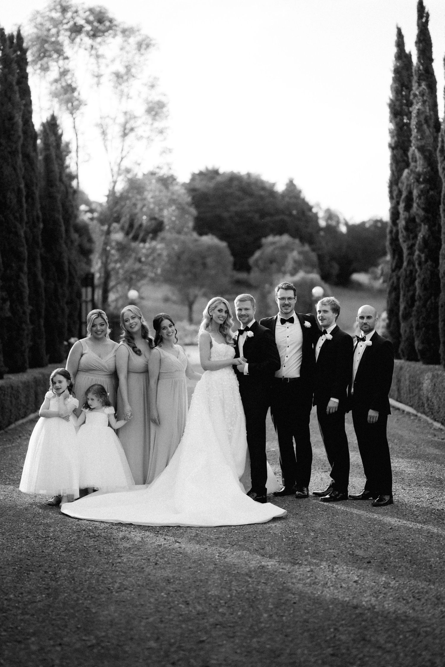 Wedding party poses for formal portrait with cypress trees in elegant black and white.