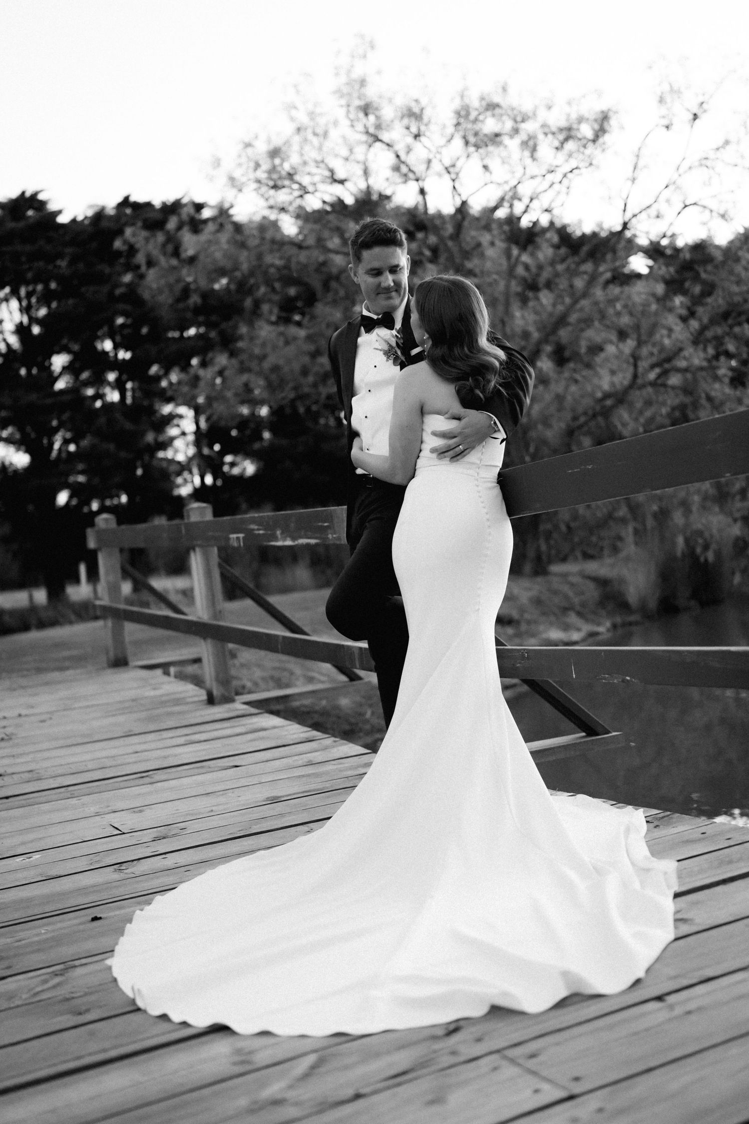 A flowing white gown spreads beautifully across wooden deck boards at sunset.