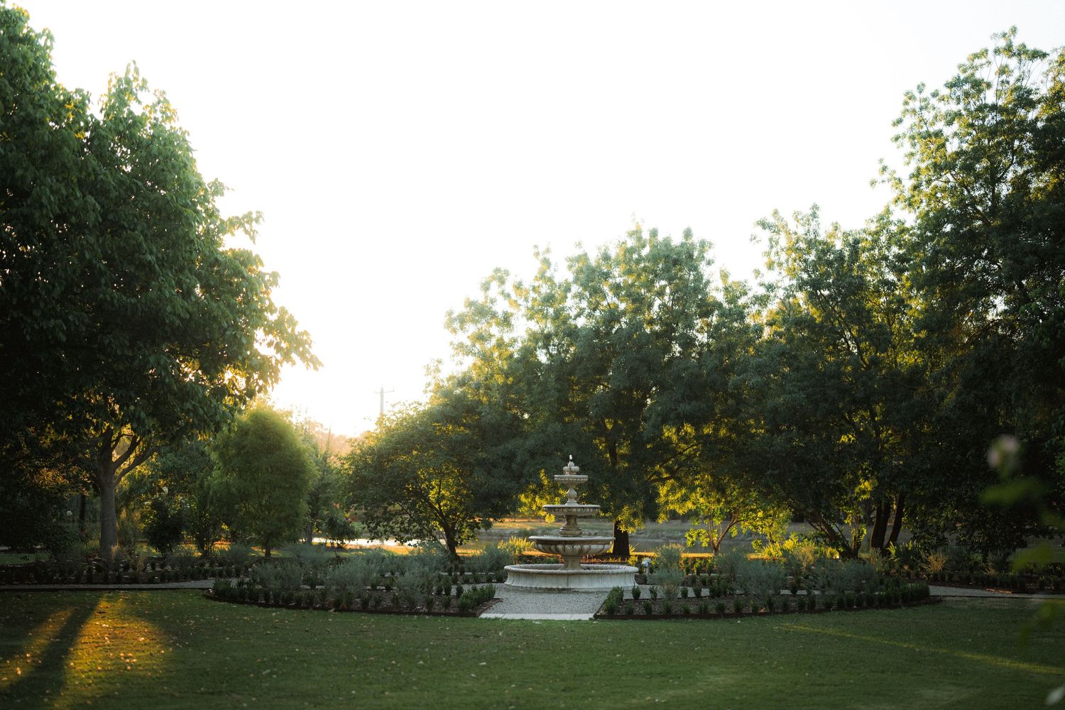 Serene garden landscape with manicured hedges and fountain at golden hour.