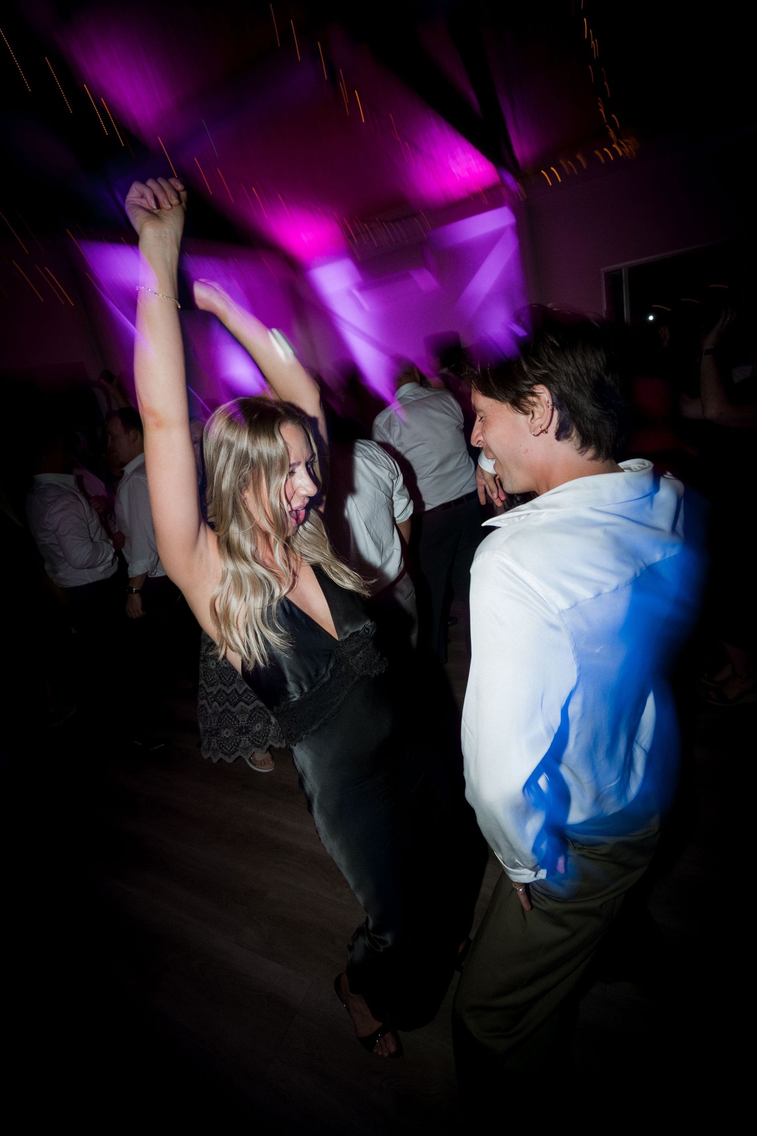 People dancing energetically under purple stage lighting at a nighttime celebration.
