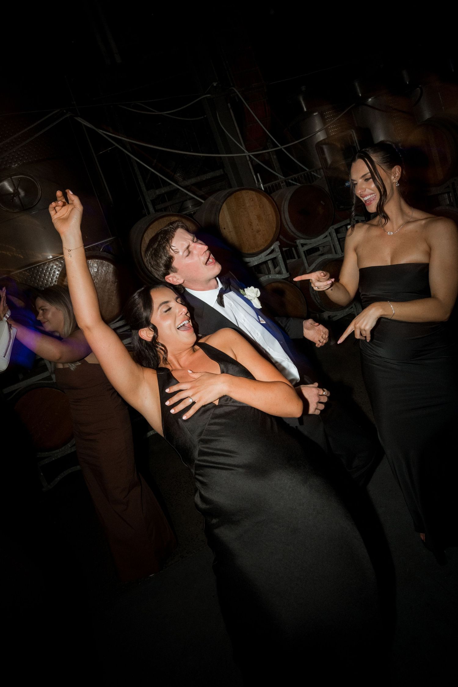 Wedding guests dance enthusiastically on a dark dance floor during a reception celebration.