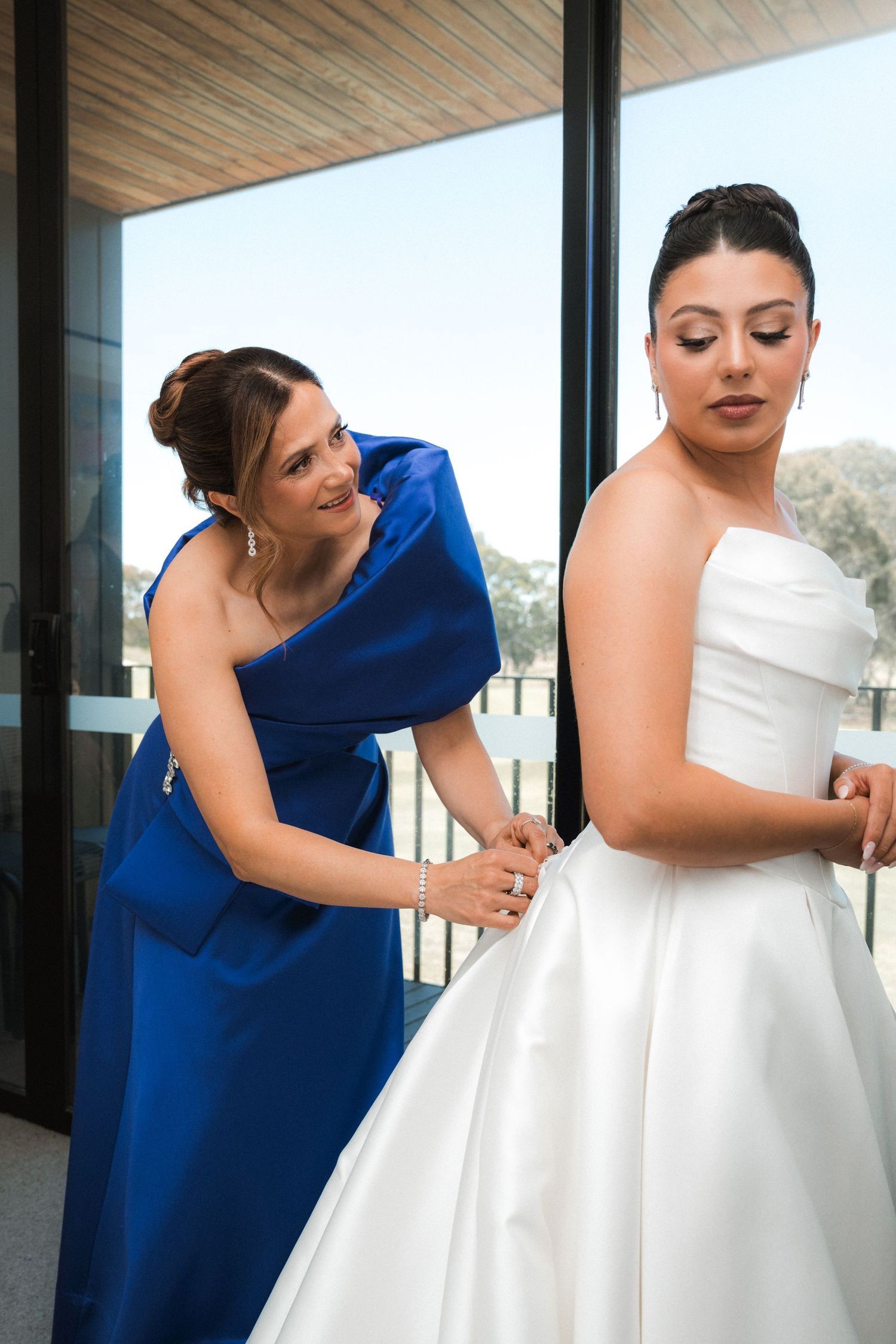 A series of photos showing a bridesmaid in royal blue helping adjust a white wedding dress.