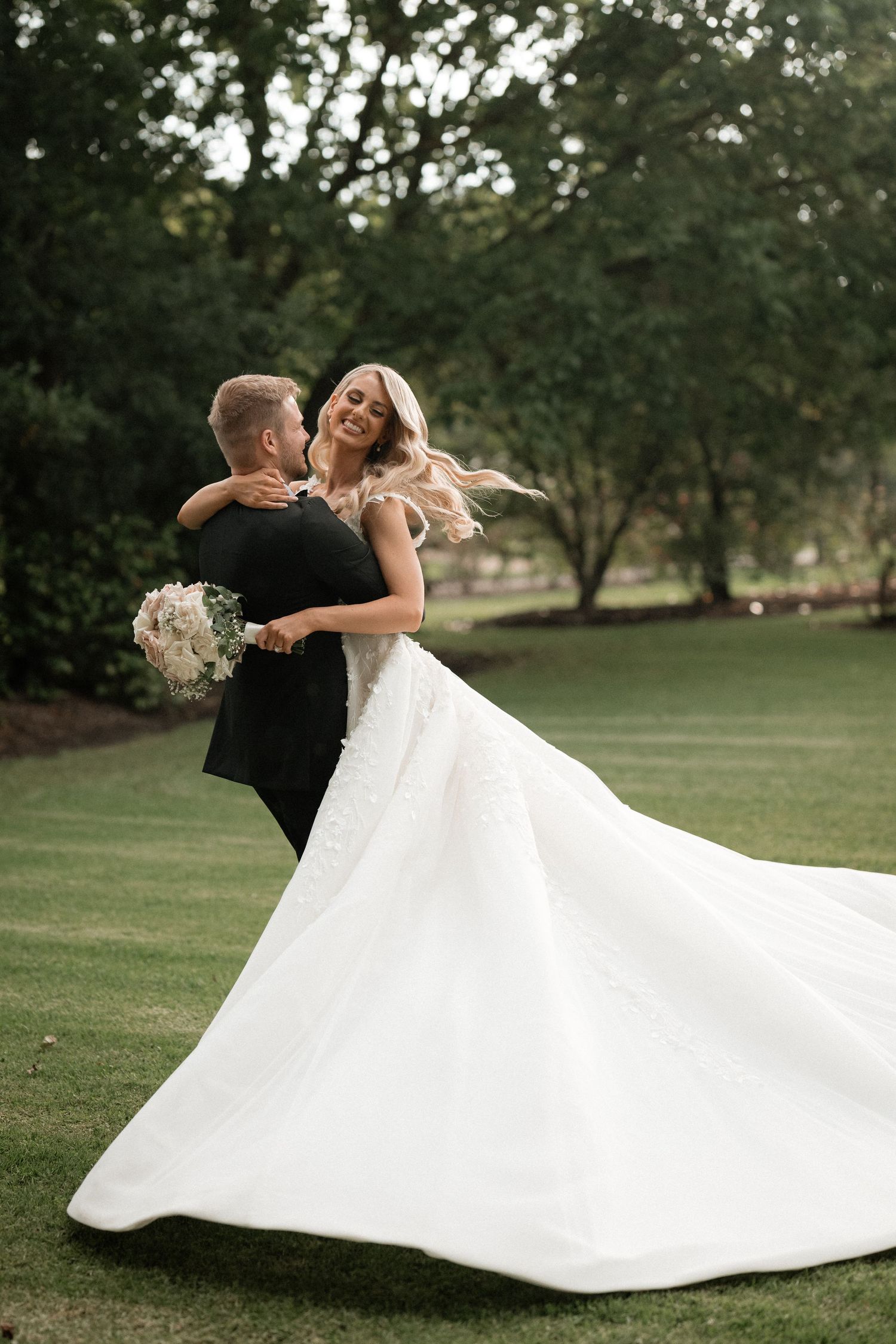 A joyful spinning dance moment between newlyweds on a grassy lawn.