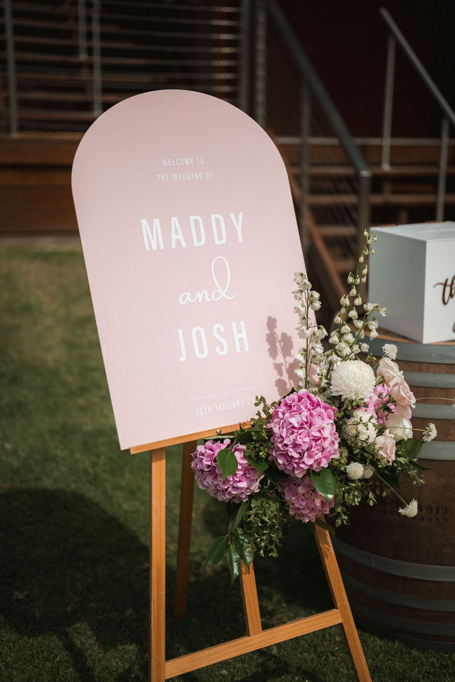Pink wedding welcome sign for Maddy and Josh decorated with pink and white floral arrangements.
