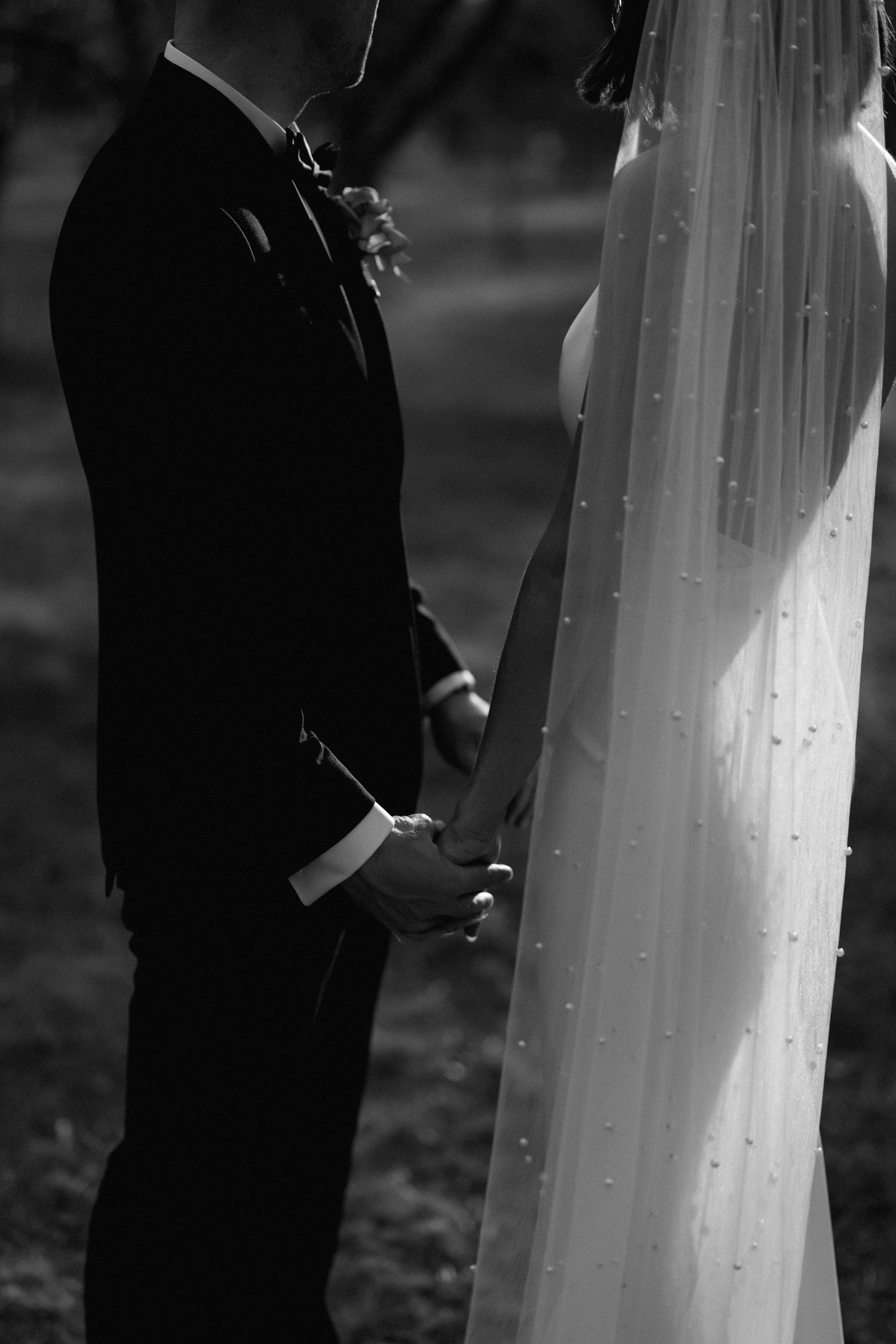 A black and white wedding photo showing a couple holding hands, with focus on the bride's flowing white dress and groom's suit.