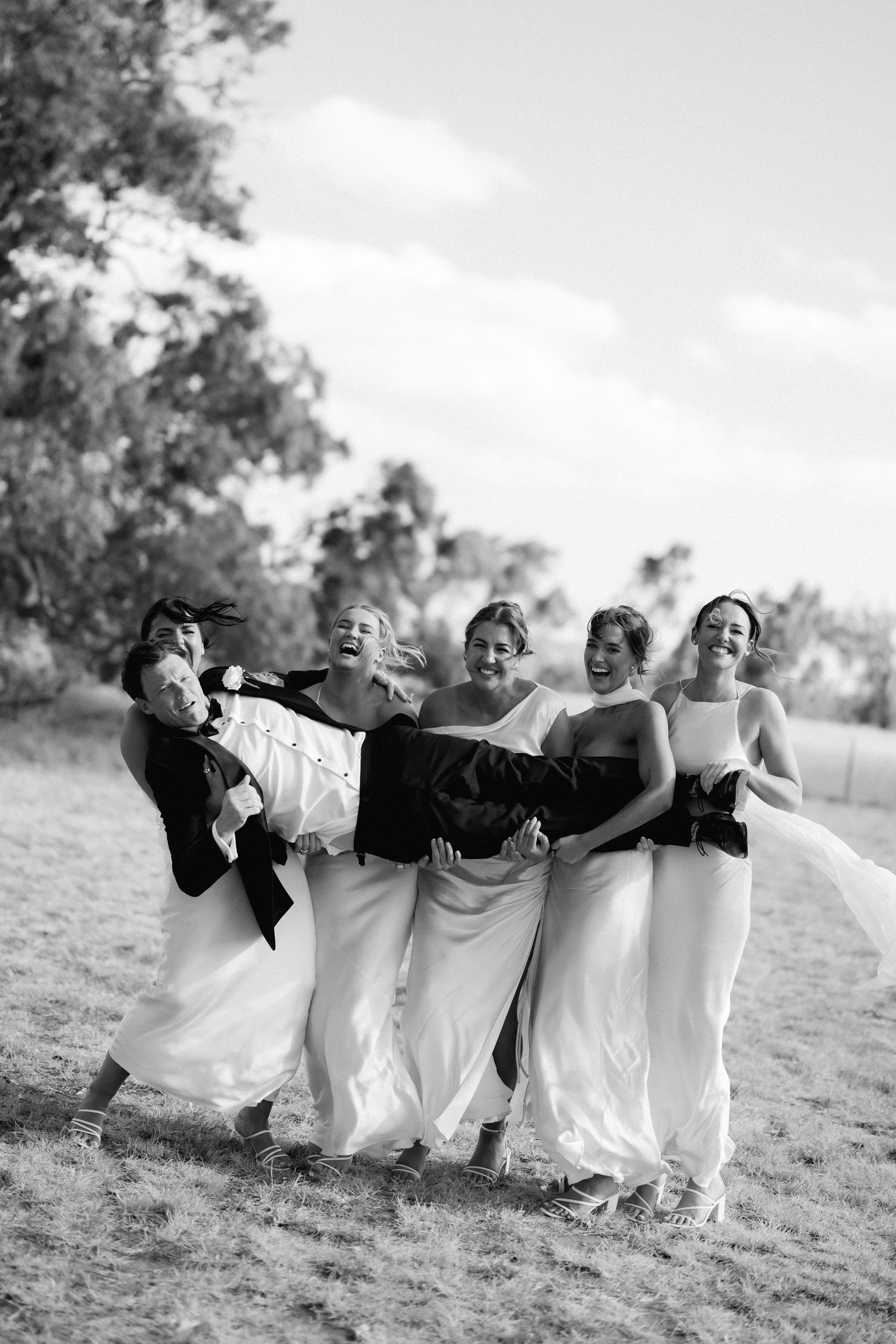 Bridesmaids in white dresses posing together on a grassy field in black and white photography.
