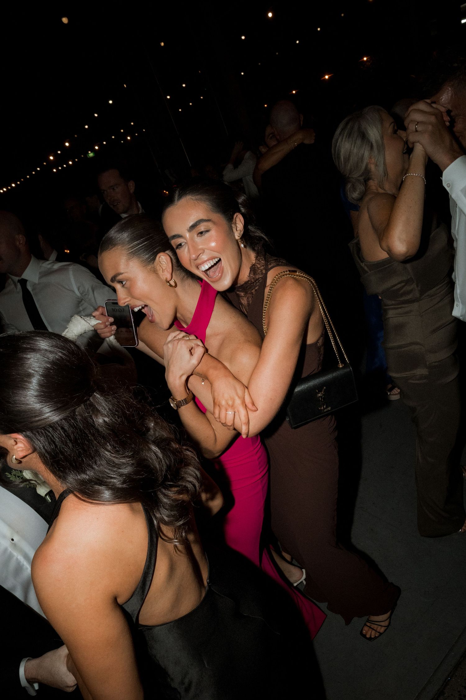 Wedding reception guests dancing and celebrating in a dimly lit venue.