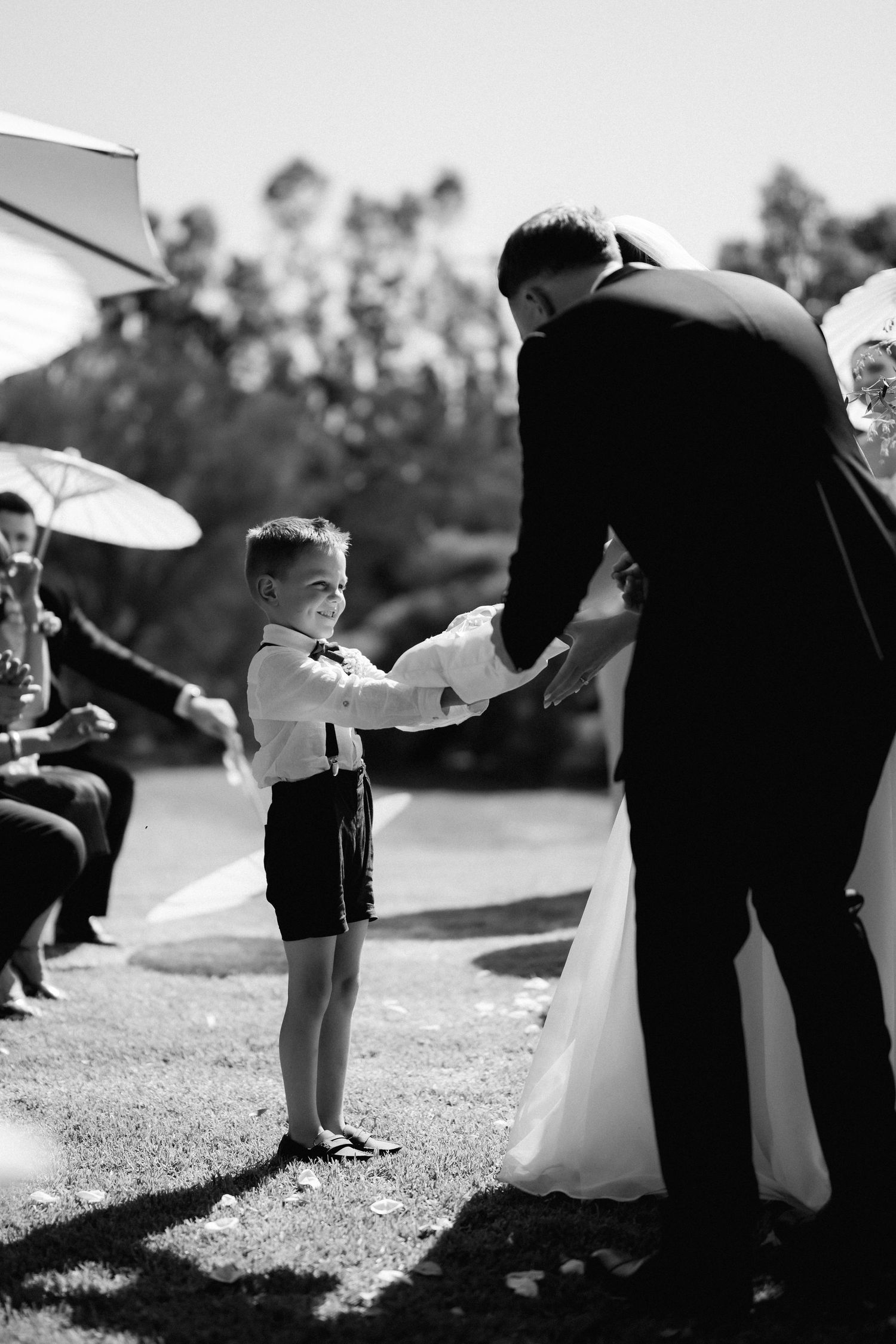 Black and white photo of wedding party members helping with dress adjustments outdoors.