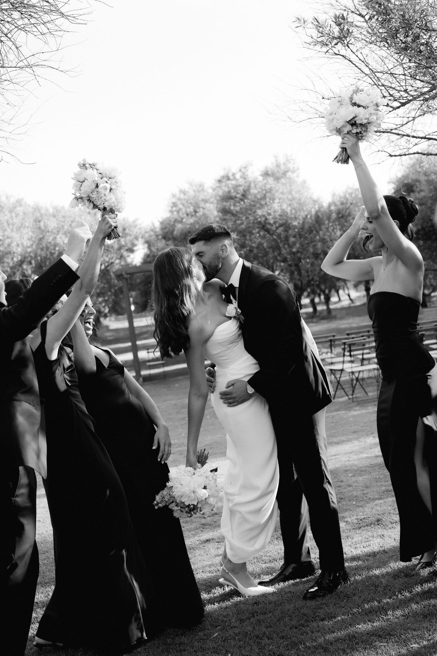 Wedding party celebrating with raised arms in joyful group poses outdoors.