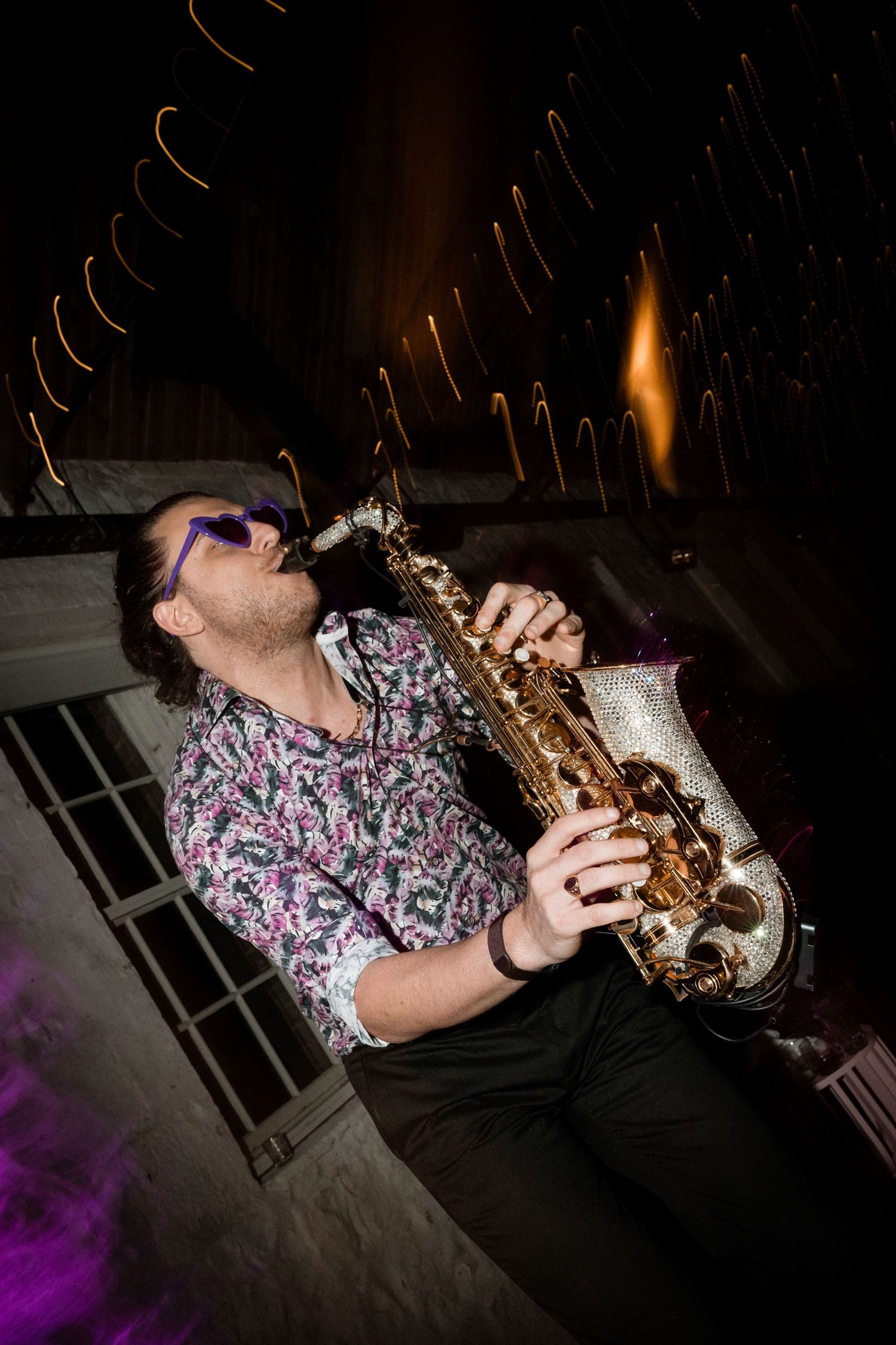 A musician plays saxophone with passion under dramatic lighting while performing at a concert.