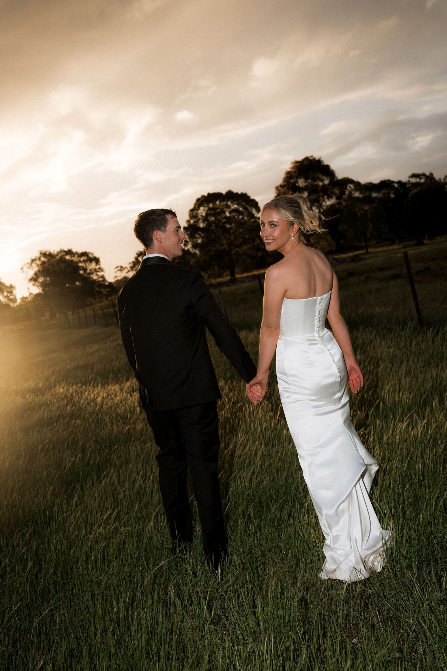 Wedding couple walking through tall grass during golden hour sunset.