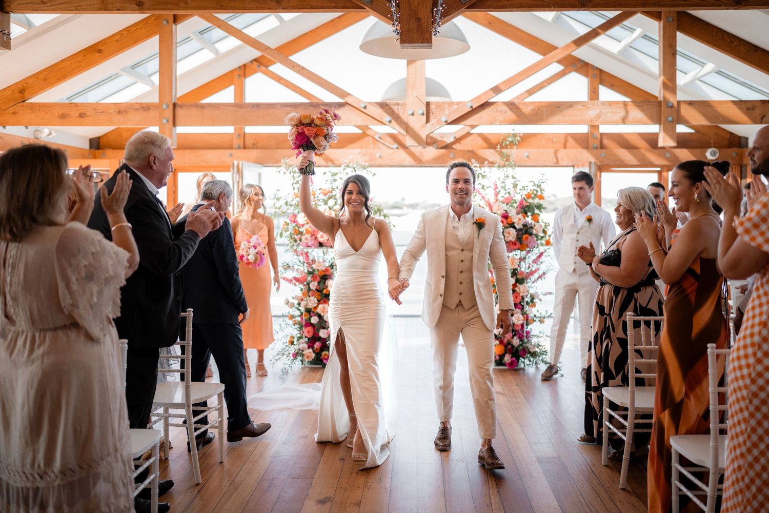 Wedding guests dance and celebrate under a rustic wooden beam ceiling with string lights.
