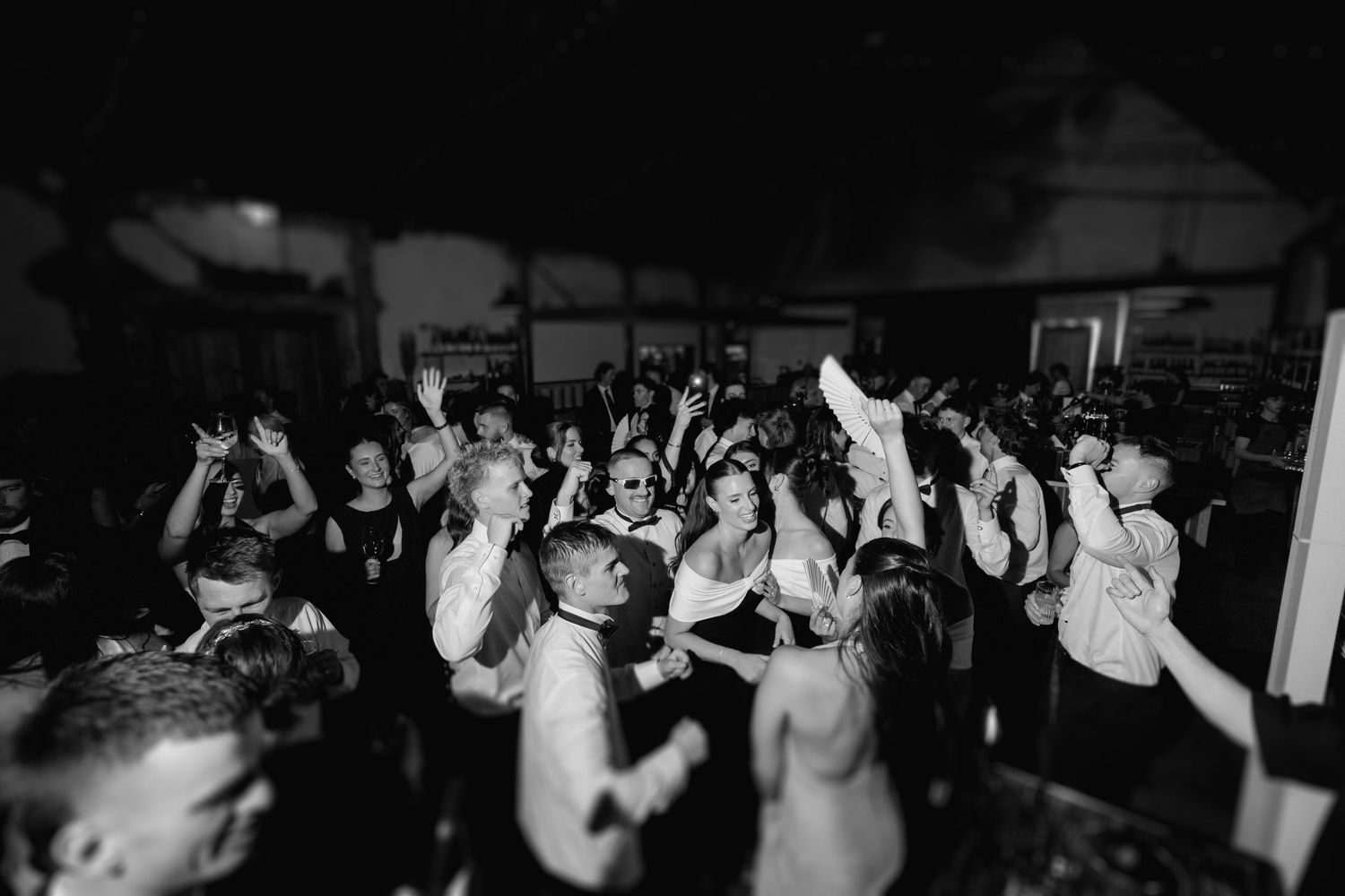 A black and white photo shows a crowd with raised hands dancing at a nightclub or party event.