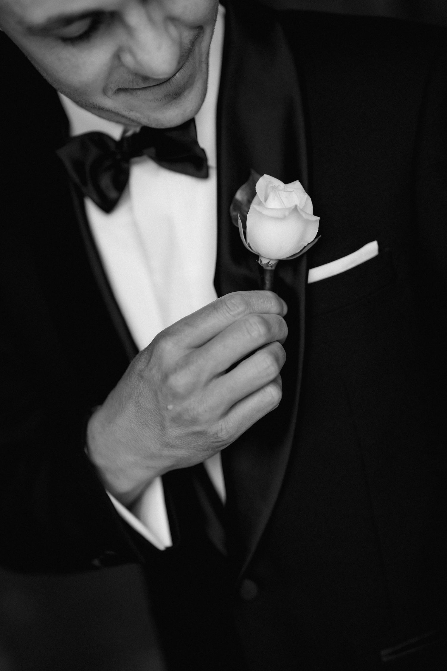 Close-up of boutonniere being pinned on black tuxedo jacket.