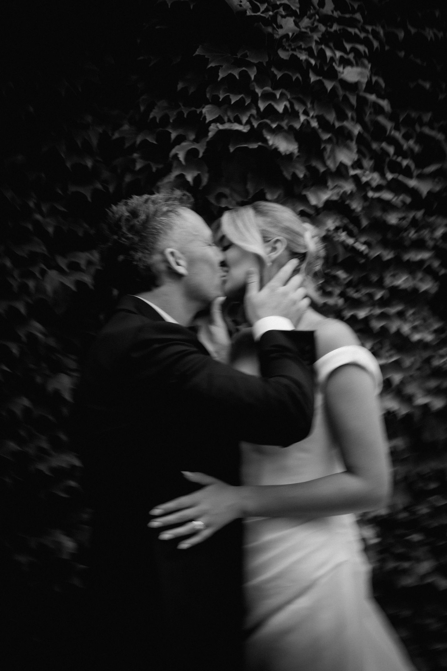 Romantic black and white portrait of couple embracing against ivy wall.
