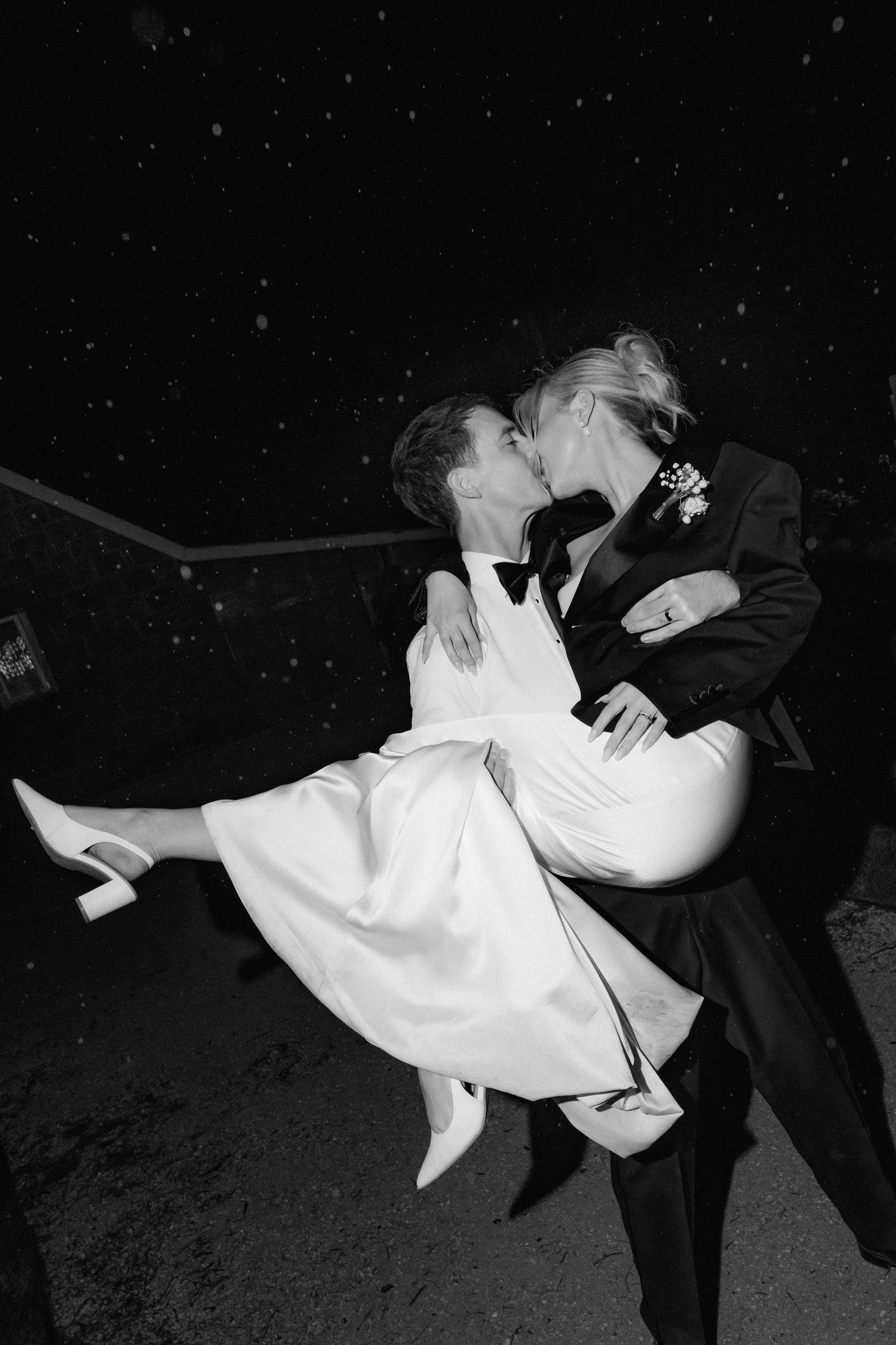 Romantic black and white photo of couple in formal wear dancing under starlit sky.