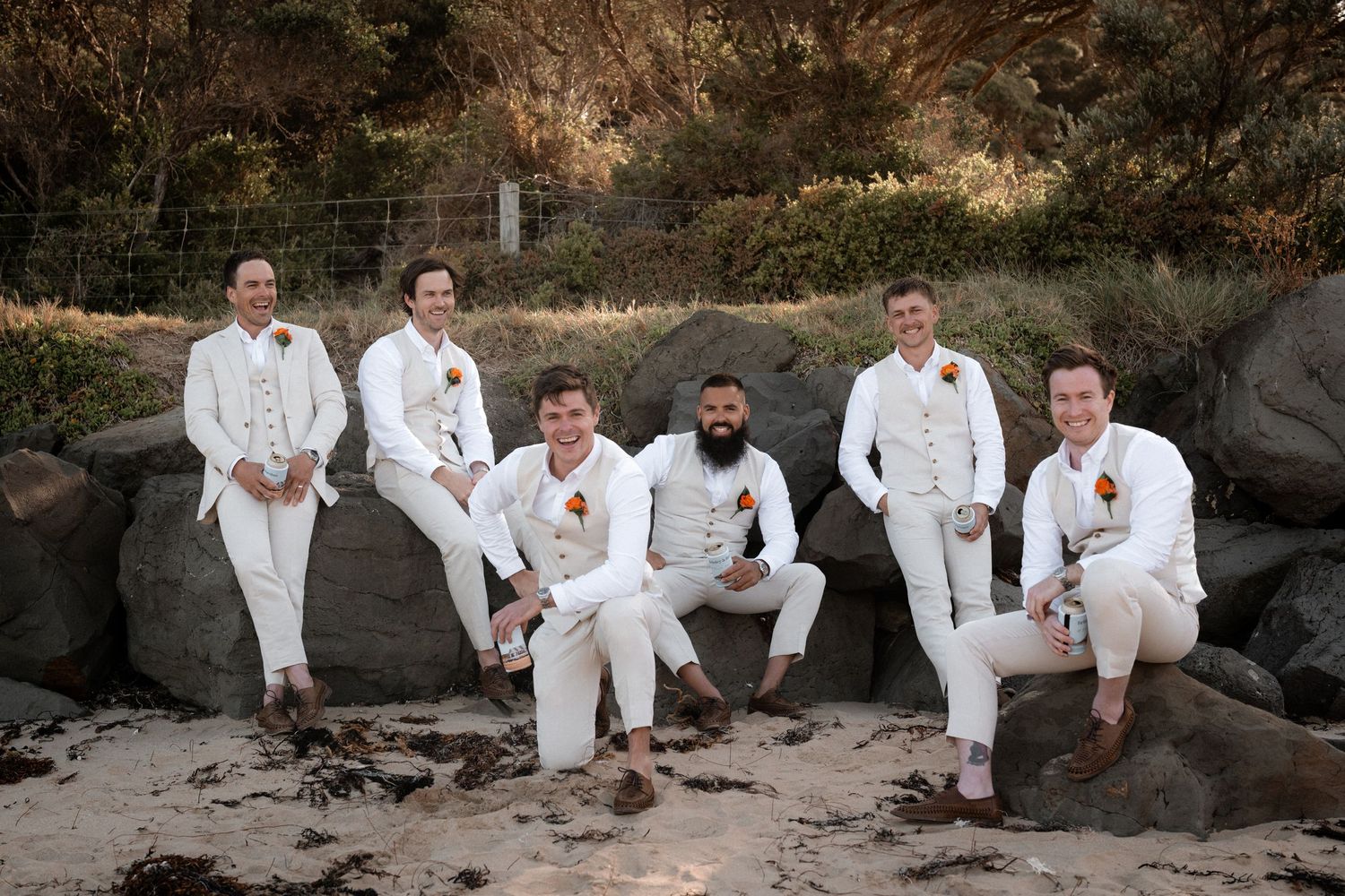 A group in white attire sitting together on coastal rocks at sunset.