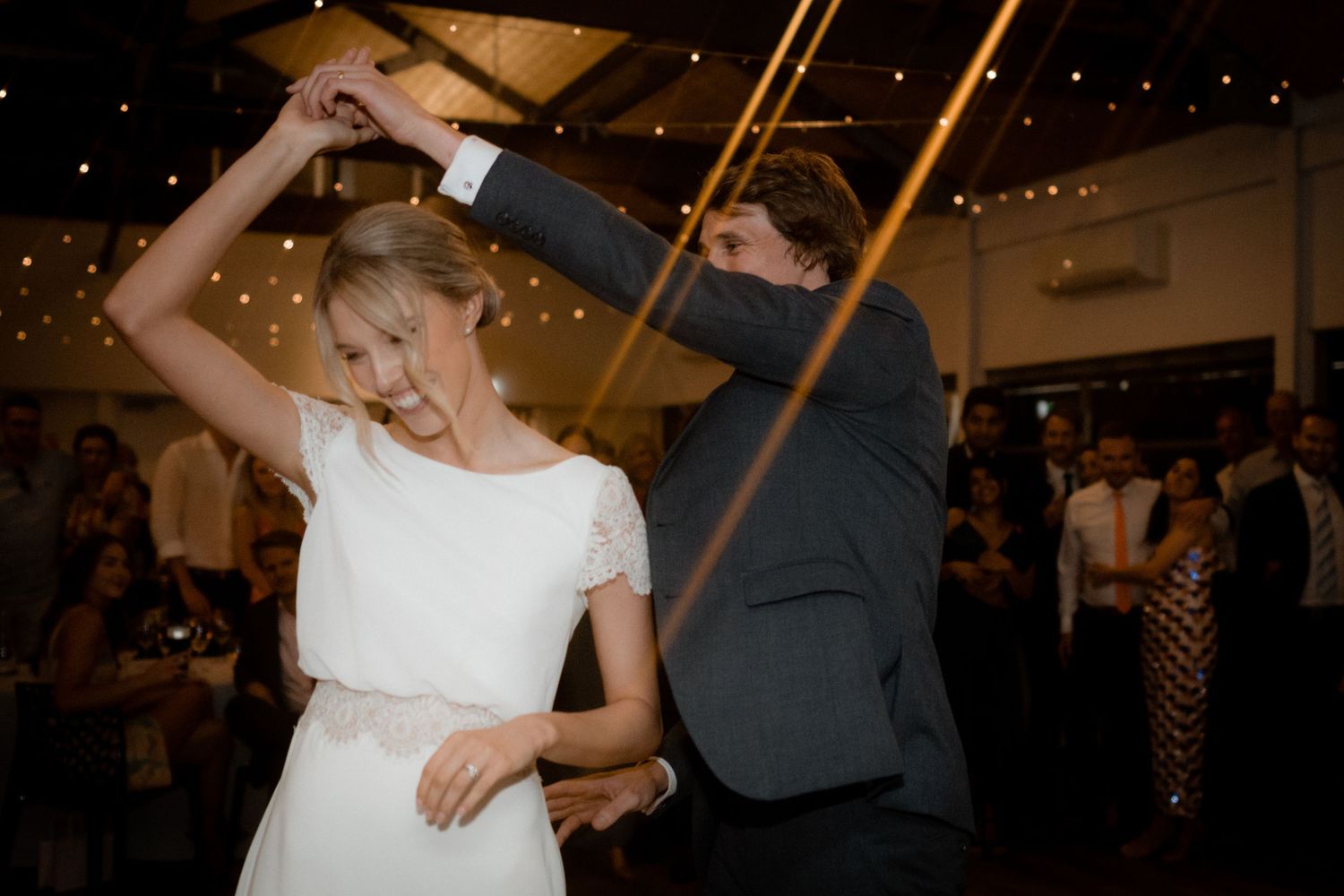 A couple dances together under warm lights during their wedding reception.