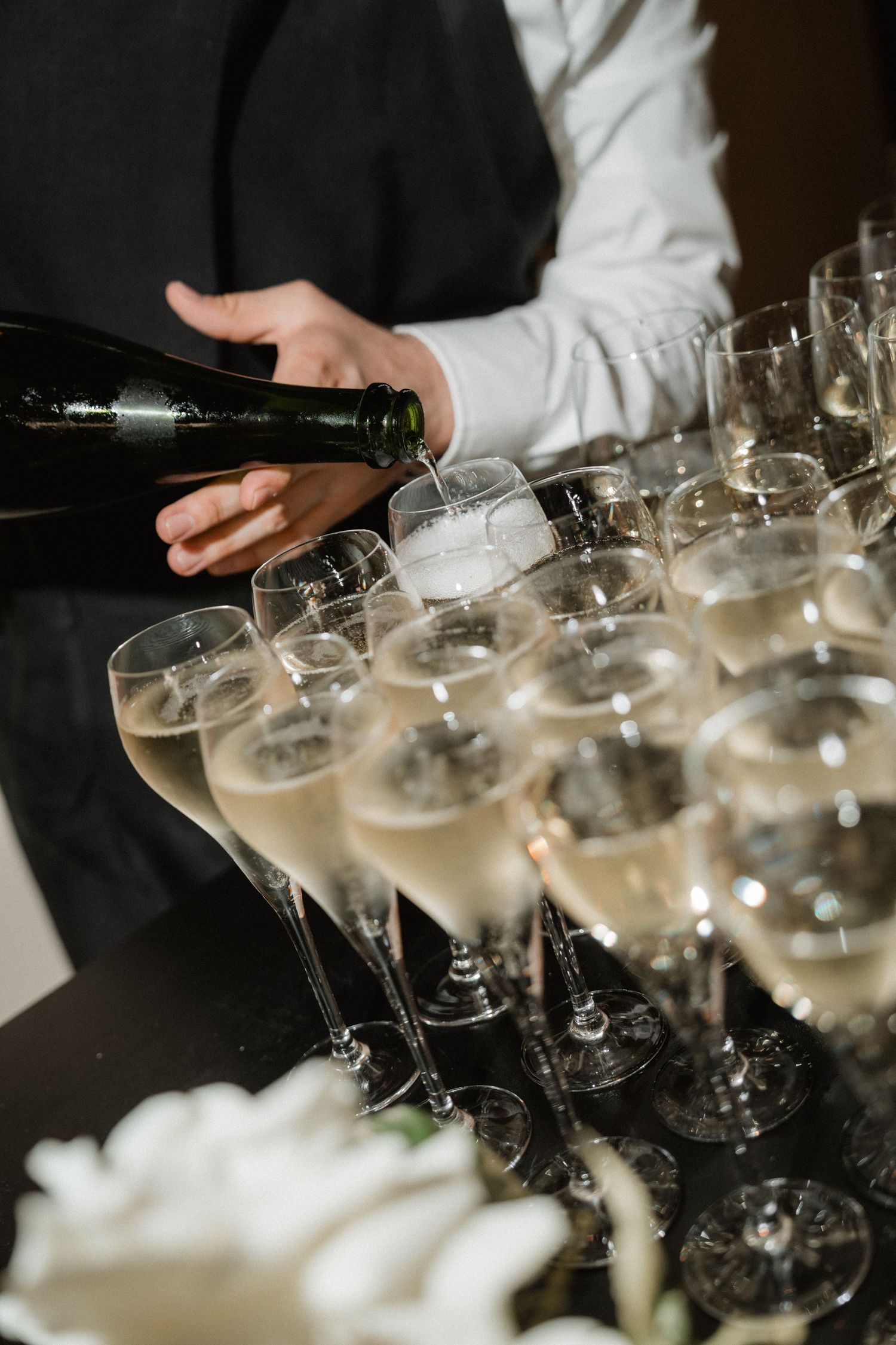 A server pours champagne into elegant crystal glasses arranged on a table during an upscale event service.