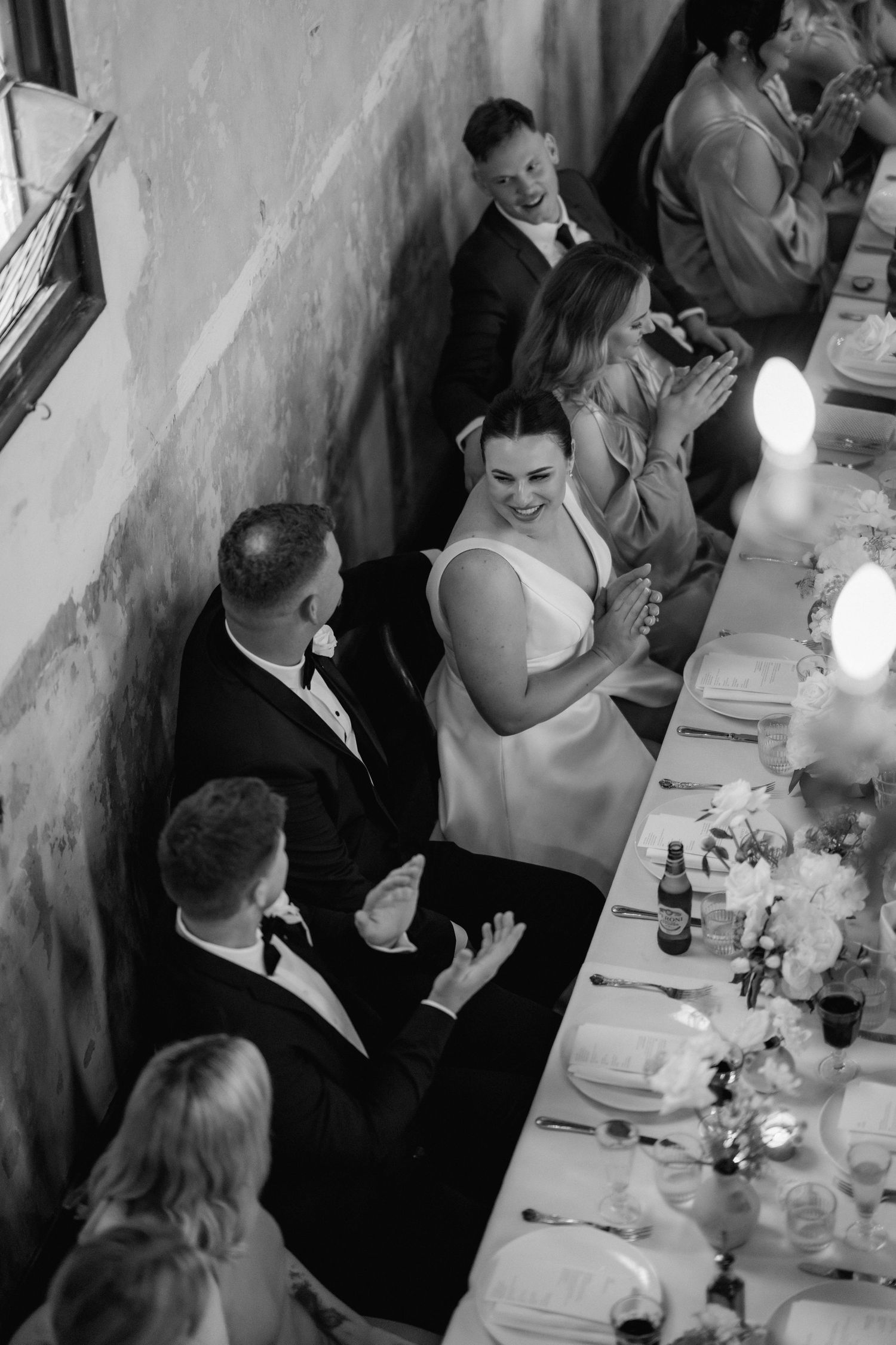 Wedding reception guests in formal attire gathered around long dining table during celebrations.