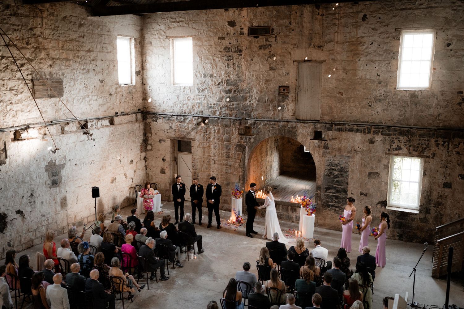Wide angle view of a wedding ceremony in a historic stone building with natural light.