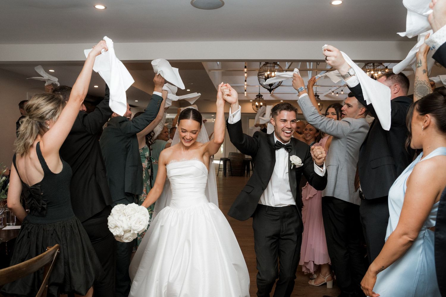 Wedding guests dance and celebrate with raised arms at a lively reception party.
